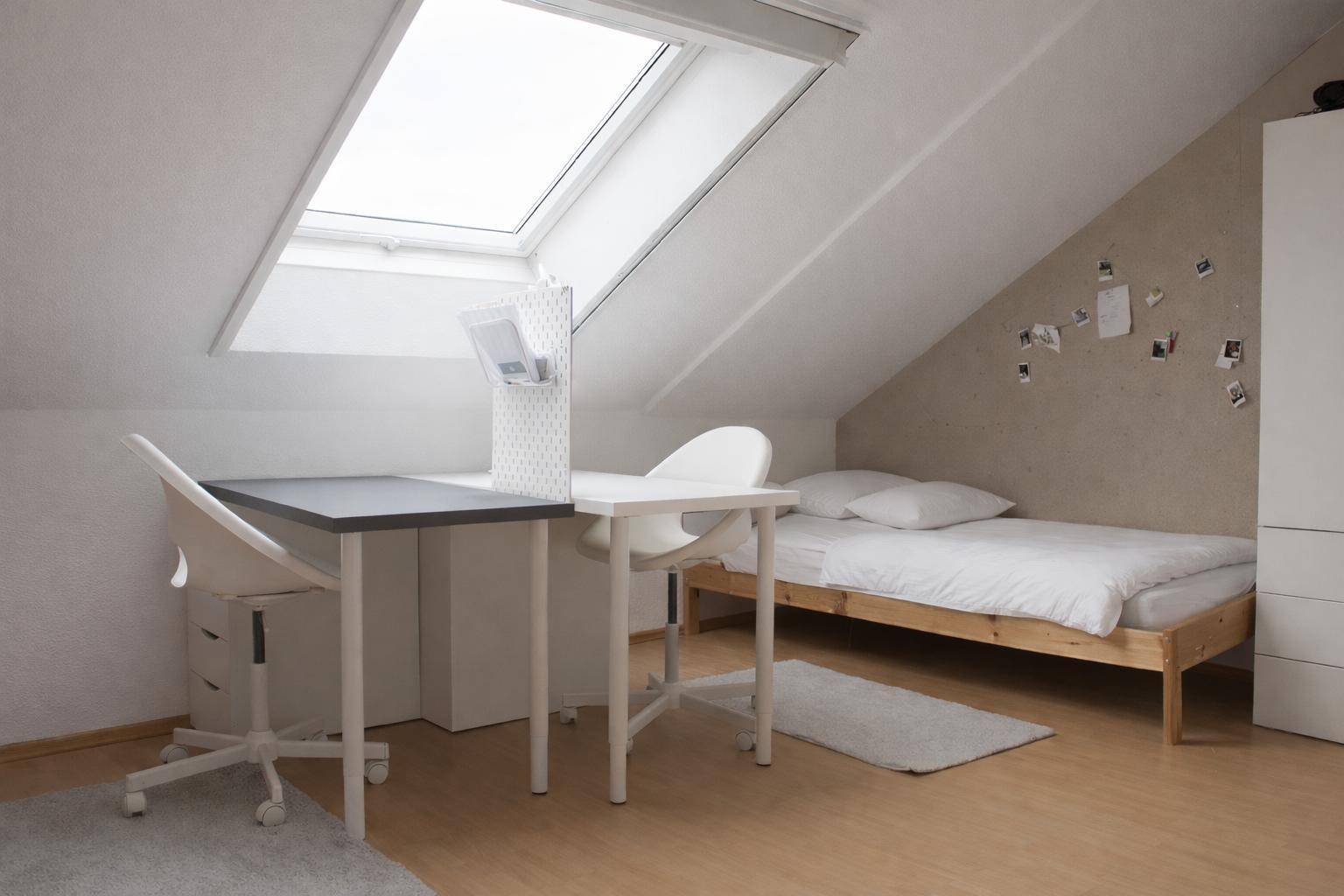 Helles Schlafzimmer im Dachgeschoss mit Dachfenster, Bett und Schreibtisch.