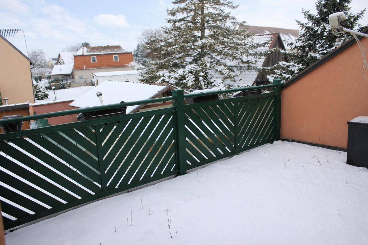 Balkon im Winter mit Schnee, grüner Holzverkleidung und Blick auf die Nachbarschaft.