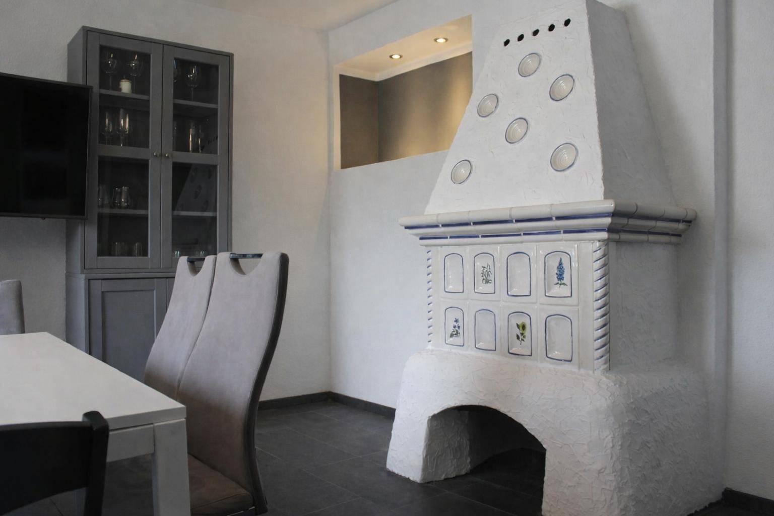 Essbereich mit traditionellem Kachelofen, Esstisch und modernem Sideboard.