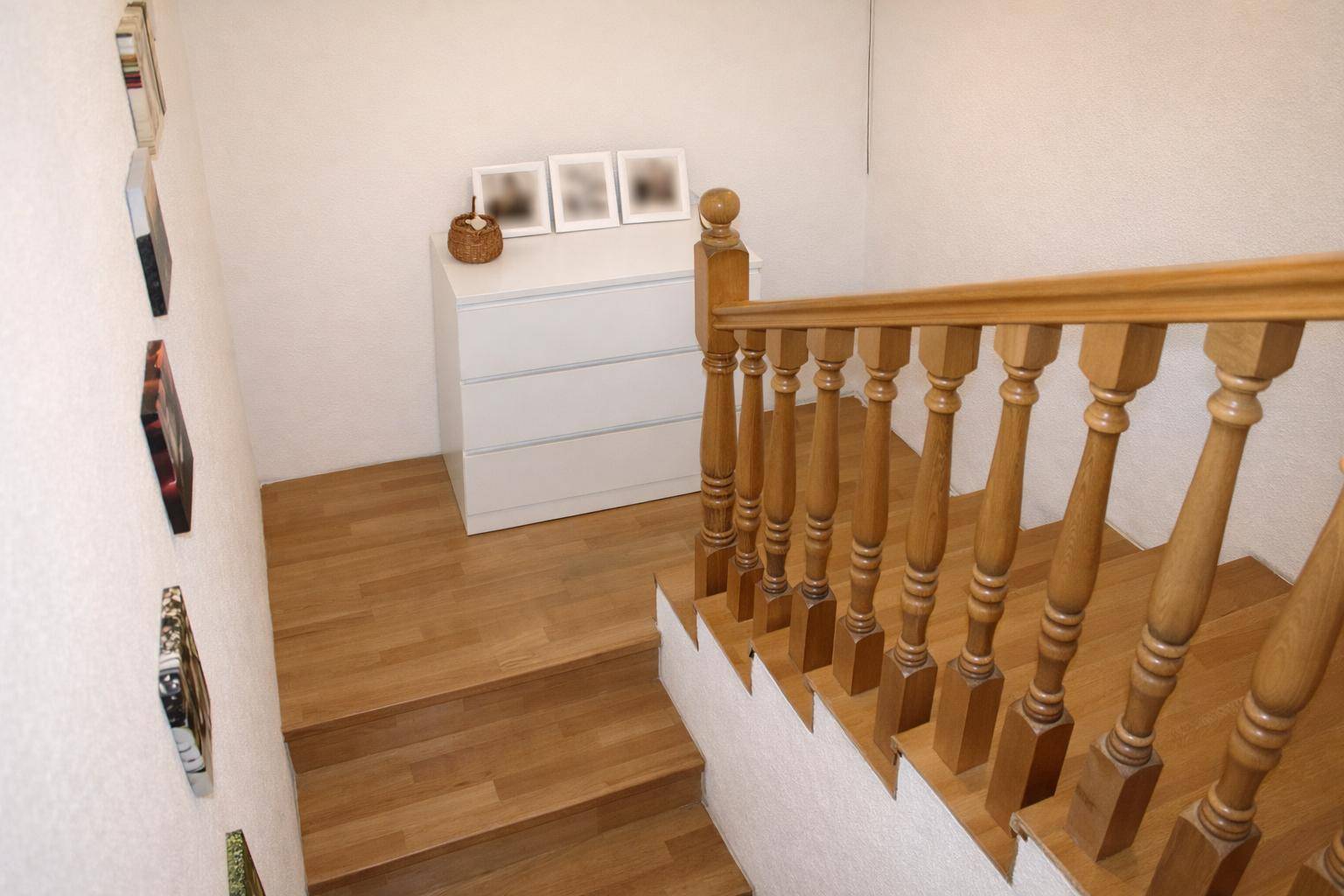 Holztreppe führt in den oberen Bereich, mit hellem Parkettboden und weißer Wand.
