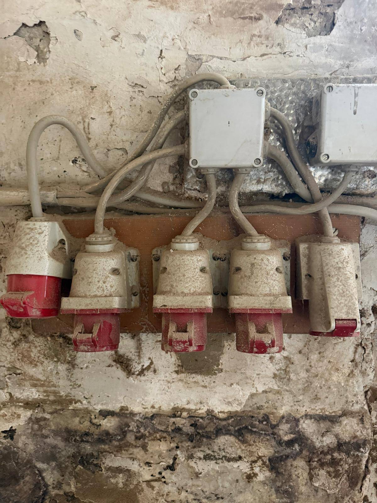 Nahaufnahme von mehreren roten Industriesteckdosen und Verkabelung an einer alten Wand.