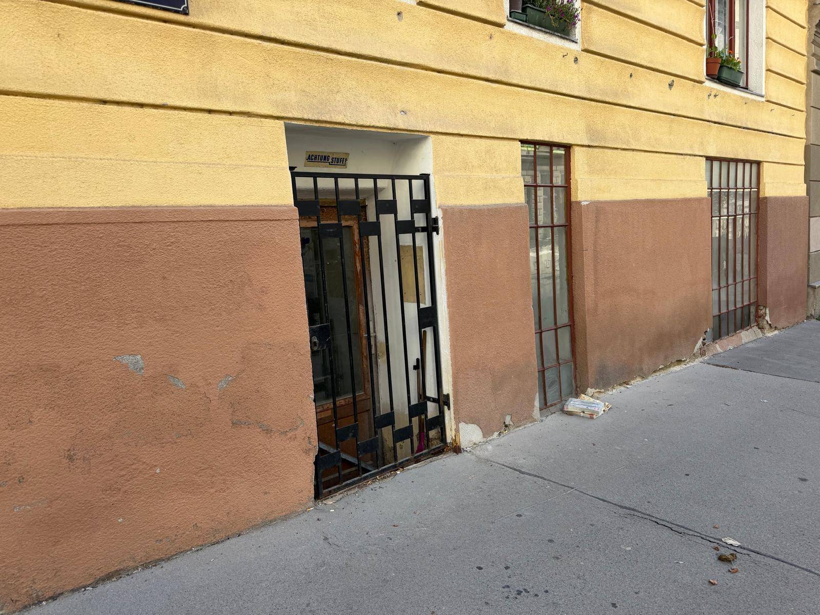 Gelb-braune Fassade eines Gebäudes mit Fenstern und einem Eingang auf Straßenniveau.