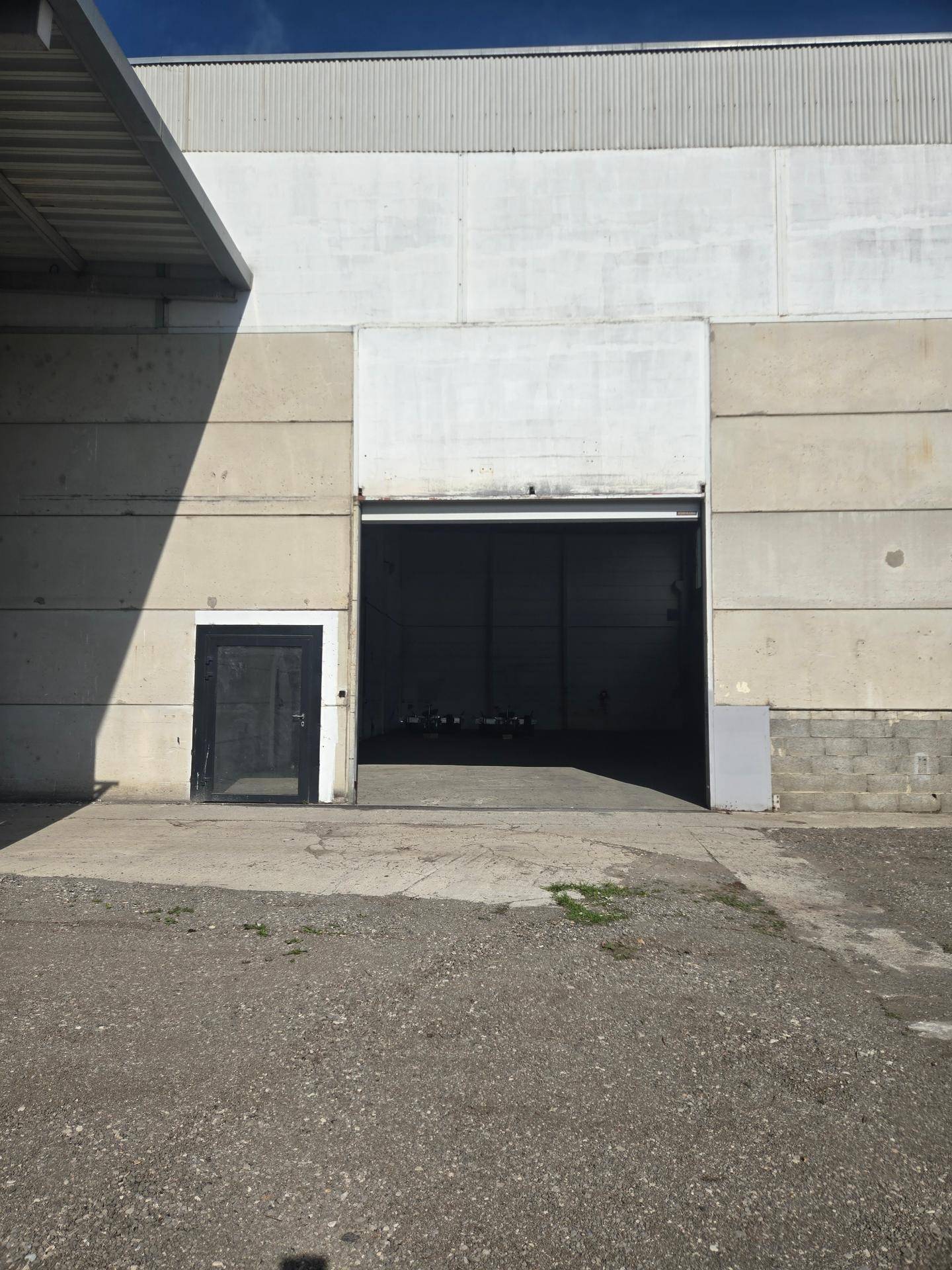 Außenansicht einer Industriehalle mit großem Rolltor für Fahrzeuge und separatem Eingangsbereich für Personen.
