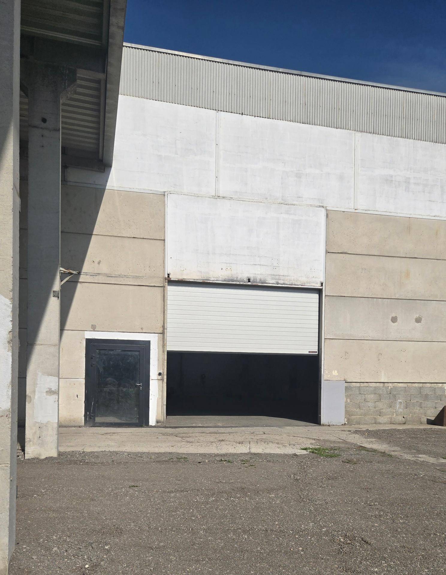 Außenansicht der Industriehalle mit teilweise geschlossenem Rolltor und separatem Eingang für den Zugang.