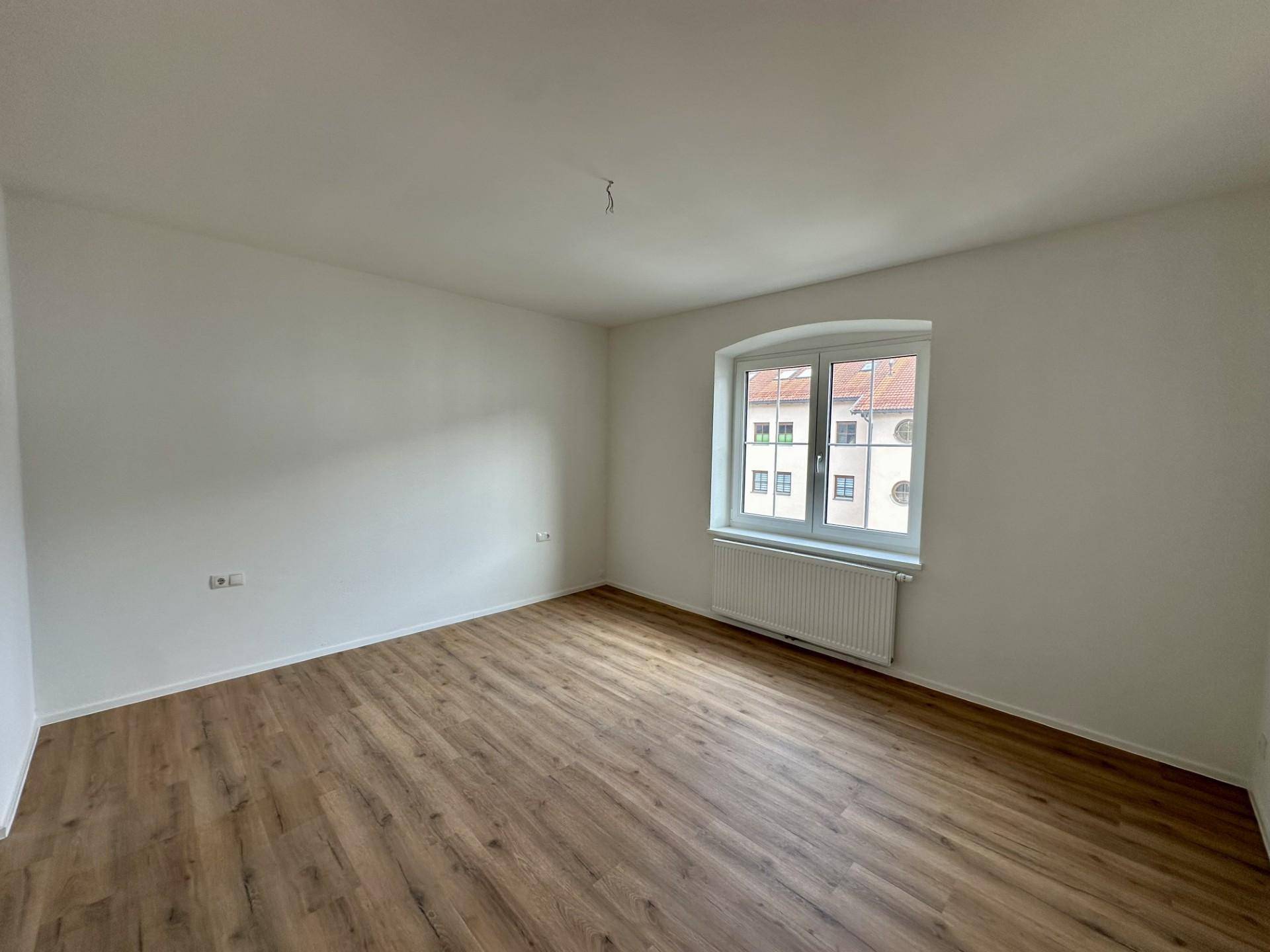 Helles Schlafzimmer mit Laminatboden und einem Fenster mit Blick auf die umliegenden Gebäude.