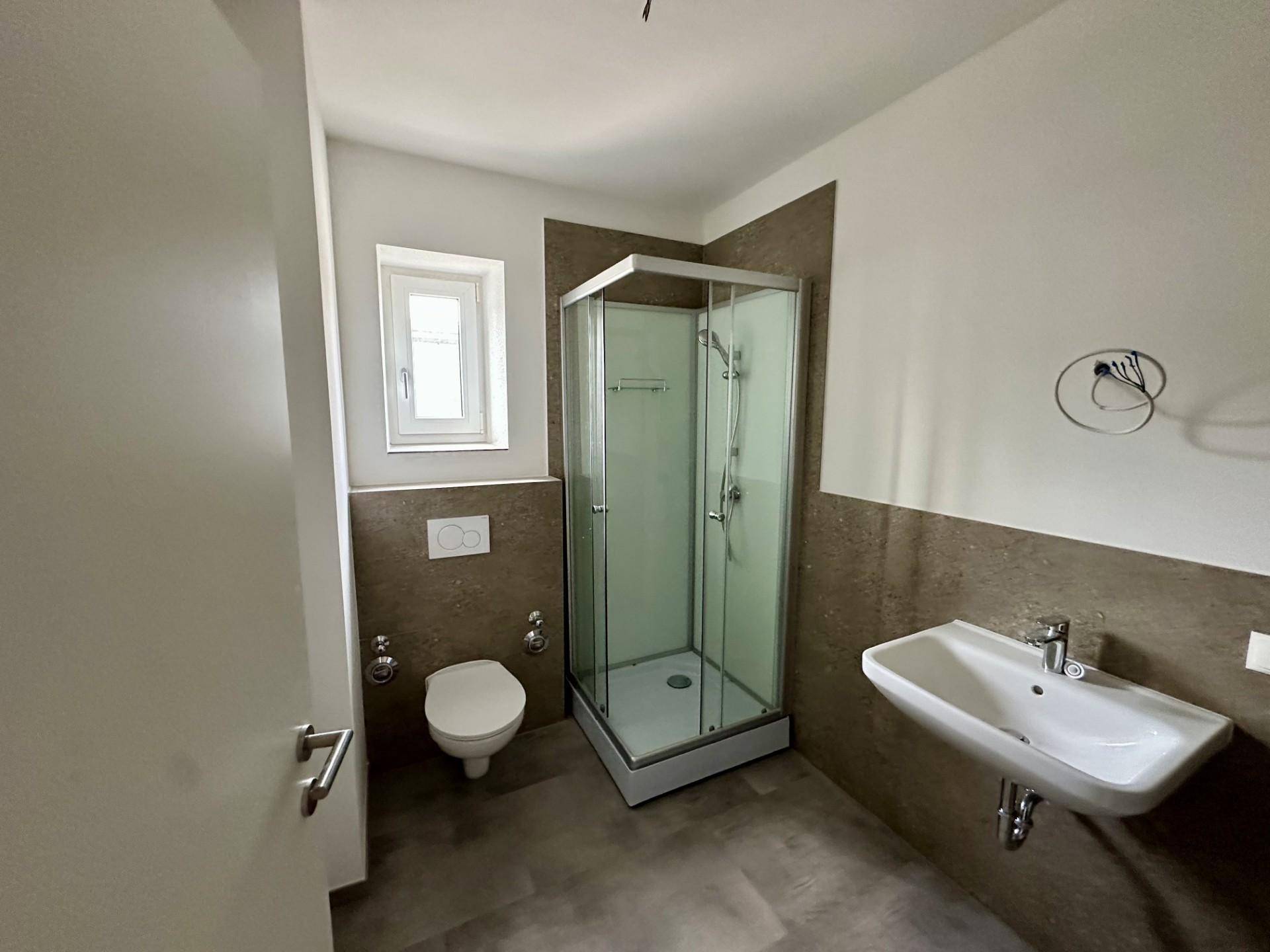 Modernes Badezimmer mit Duschkabine, WC, Waschbecken und einem Fenster für natürliches Tageslicht.