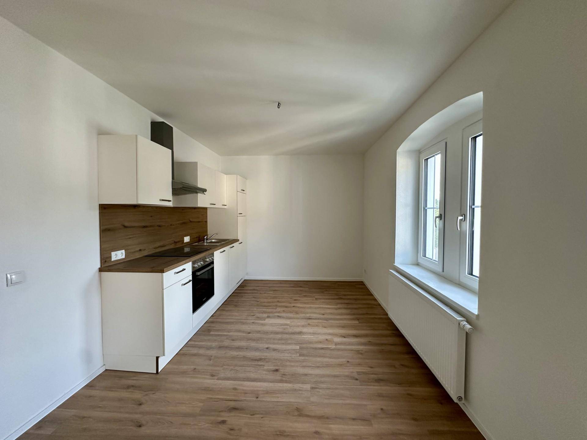 Helle Küche mit weißer Einbauküche, Holzoptik-Arbeitsplatte und Laminatboden in gutem Zustand.