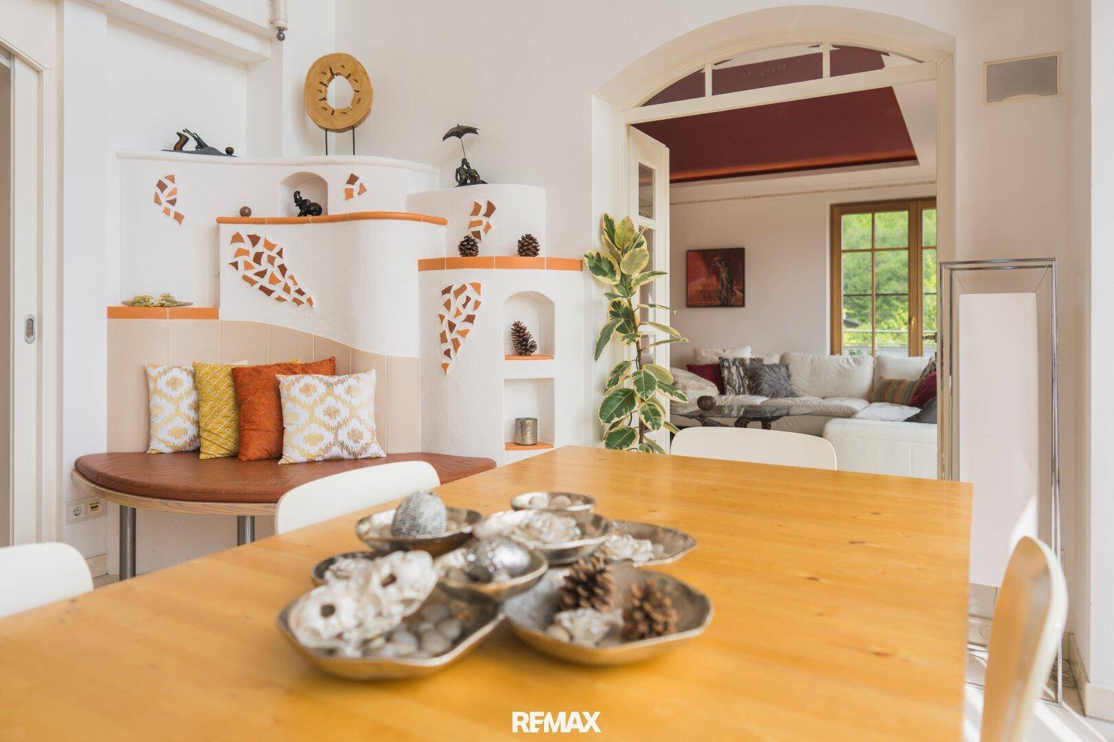 Heller Essbereich mit Holztisch und einem dekorativen Kachelofen, der zum Wohnzimmer führt.