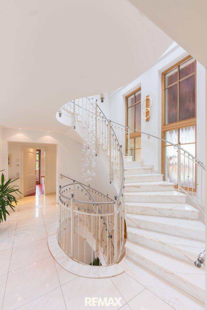 Elegantes Treppenhaus mit einer geschwungenen Marmortreppe und hohen Fenstern, die viel Licht hereinlassen.
