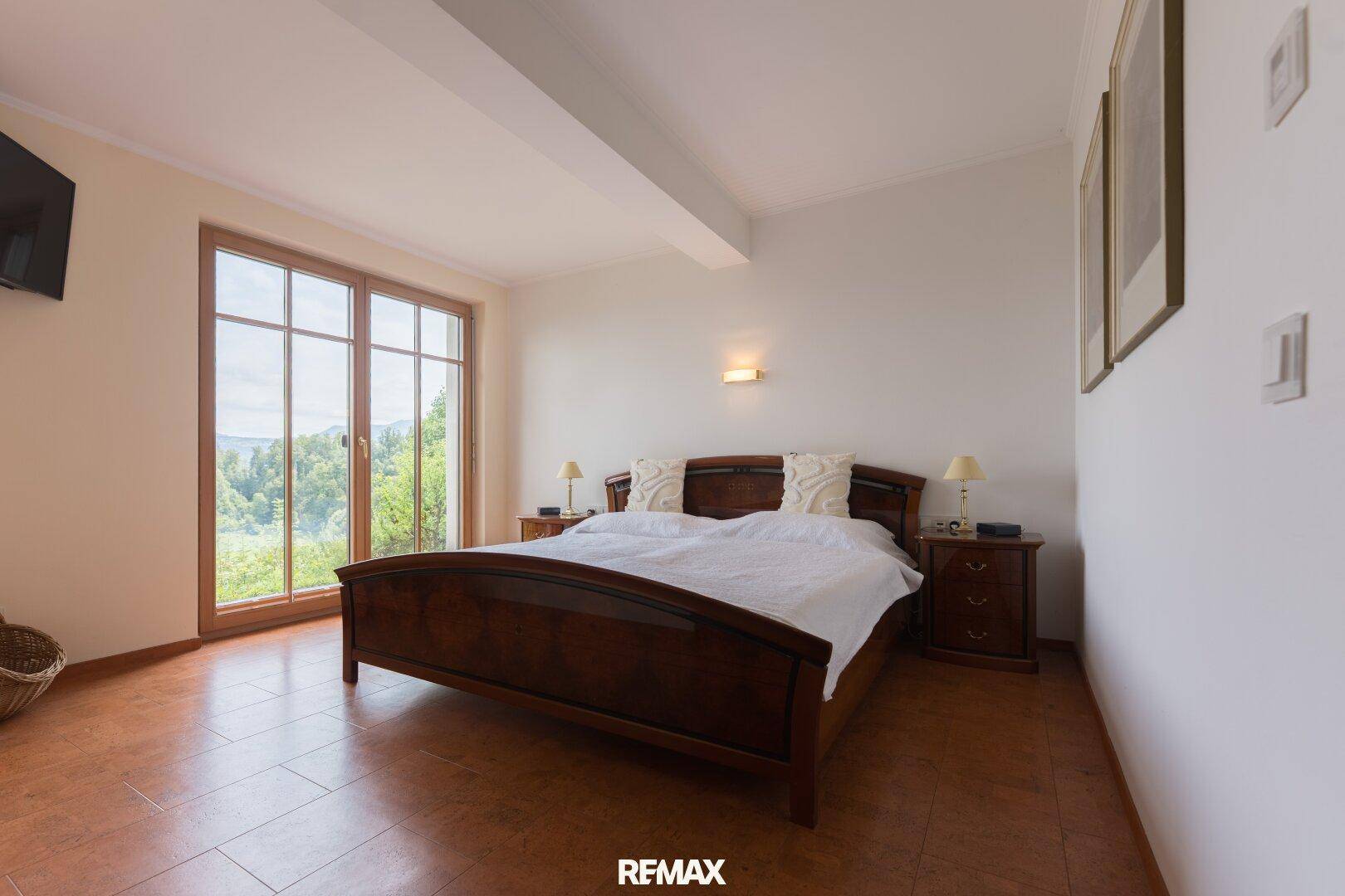 Helles Schlafzimmer mit großem Bett, Holzboden und bodentiefen Fenstern mit schöner Aussicht.