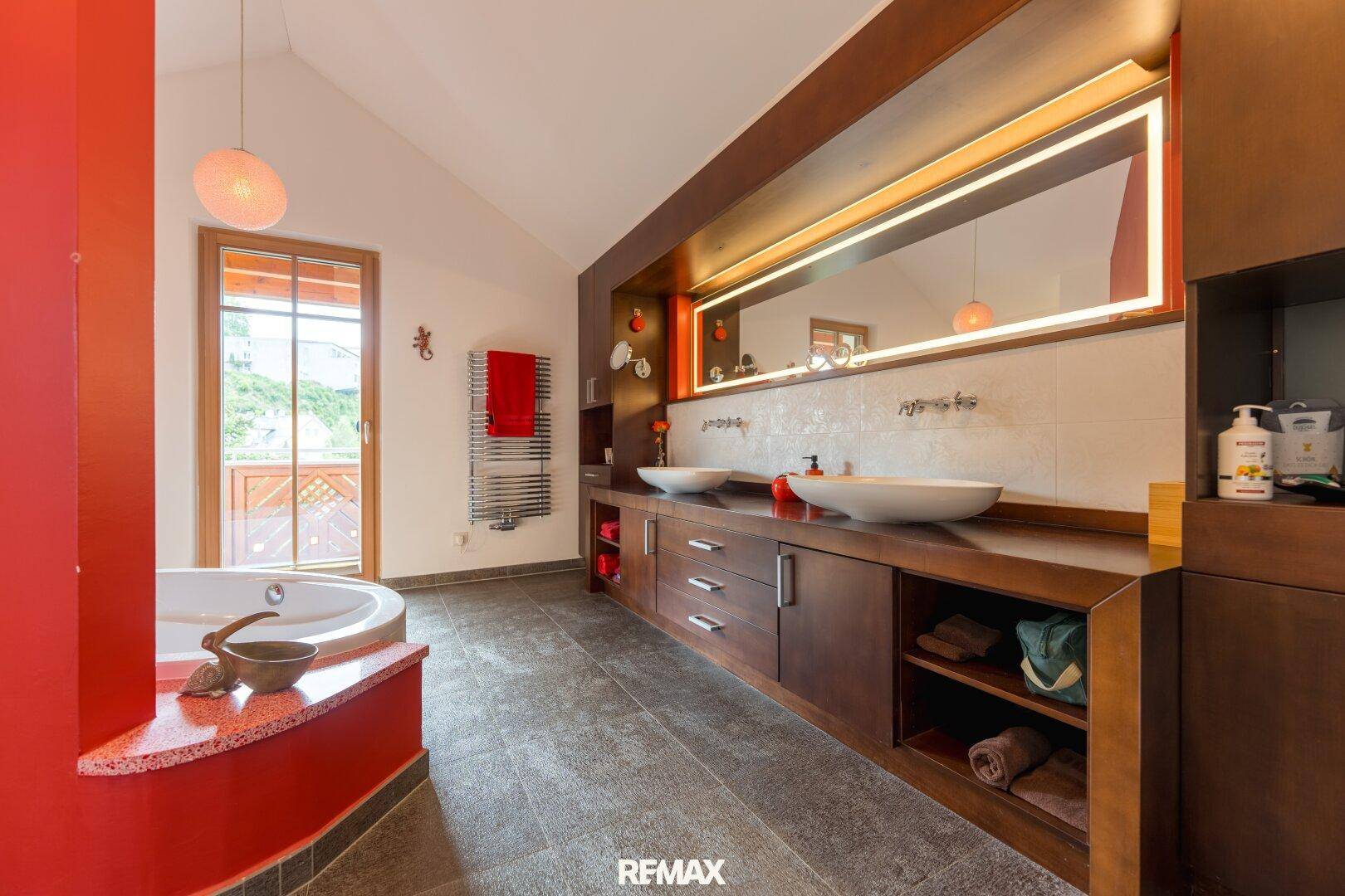 Geräumiges Badezimmer mit Doppelwaschbecken, Eckbadewanne und Zugang zu einem Balkon.