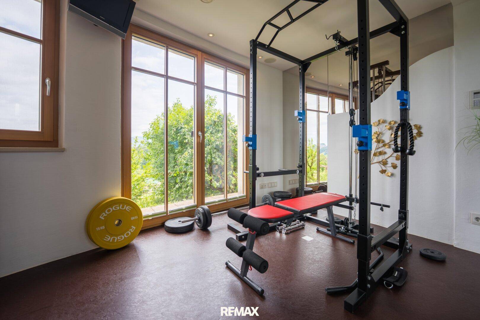 Privater Fitnessraum mit Trainingsgeräten und großen Fenstern mit Blick ins Grüne.