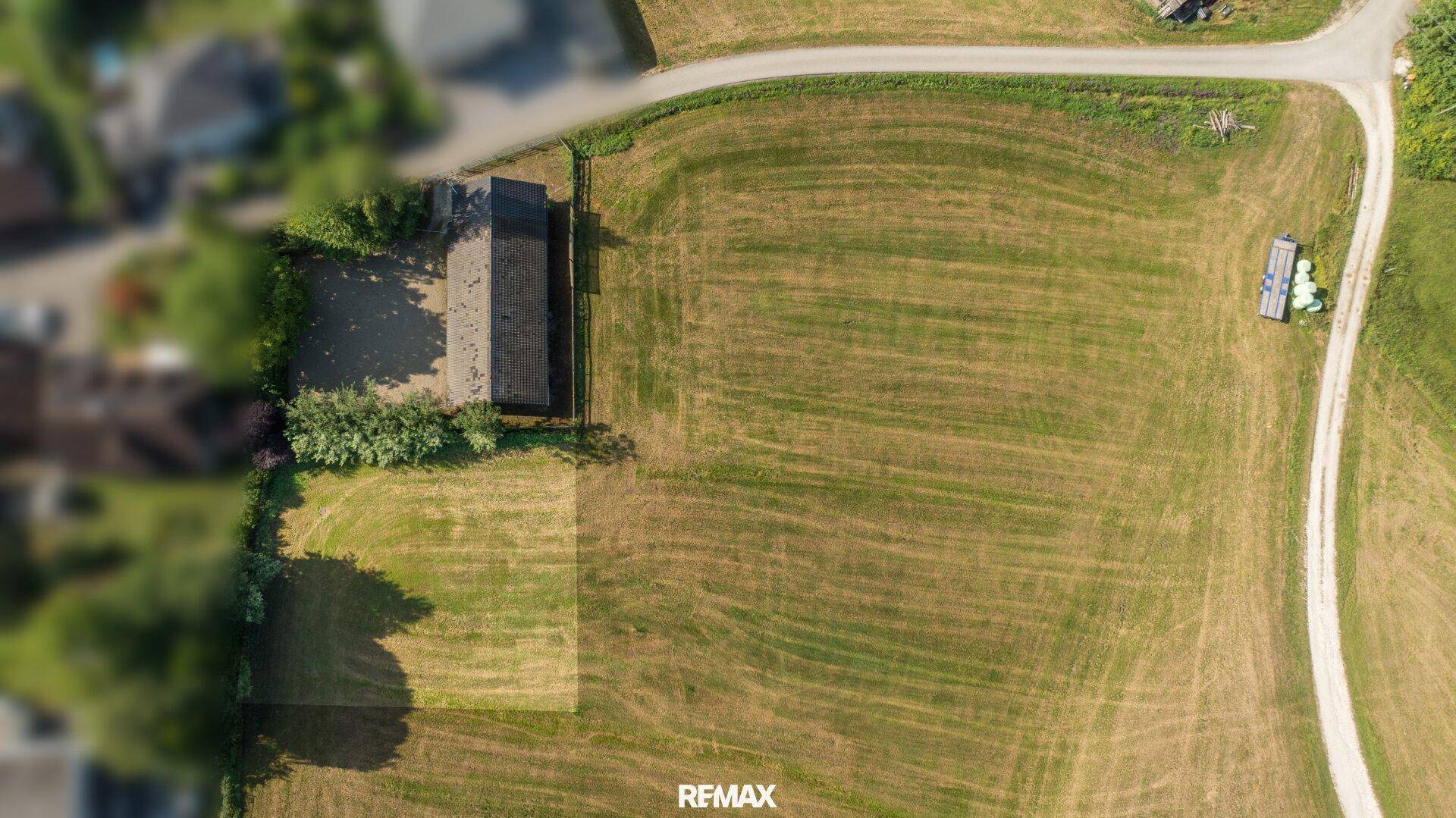 Draufsicht auf ein landwirtschaftliches Gebäude und ein umgrenztes Grundstück inmitten grüner Felder mit Zufahrtsweg.