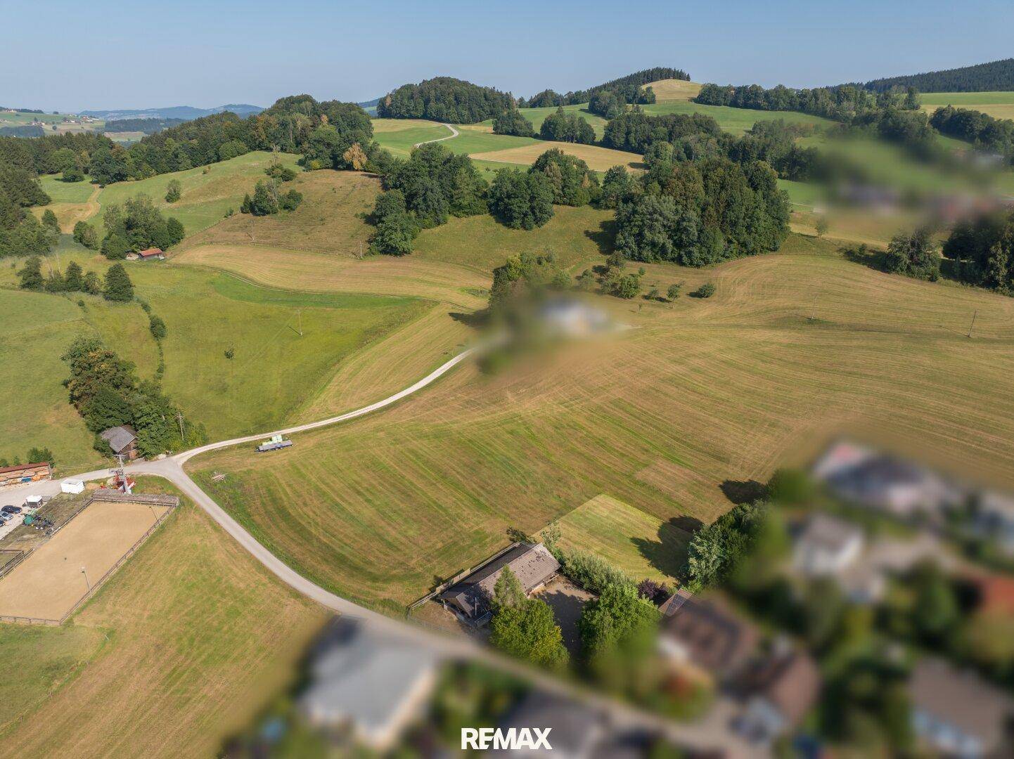 Luftaufnahme einer ländlichen Gegend mit Feldern, Hügeln und einem Anwesen mit Reitplatz und Zufahrtswegen.