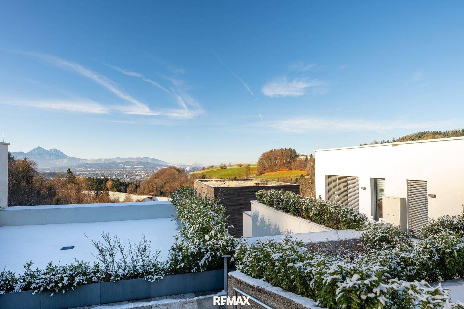 Dachterrasse mit Schnee und weitem Blick über die winterliche Landschaft und die Berge.