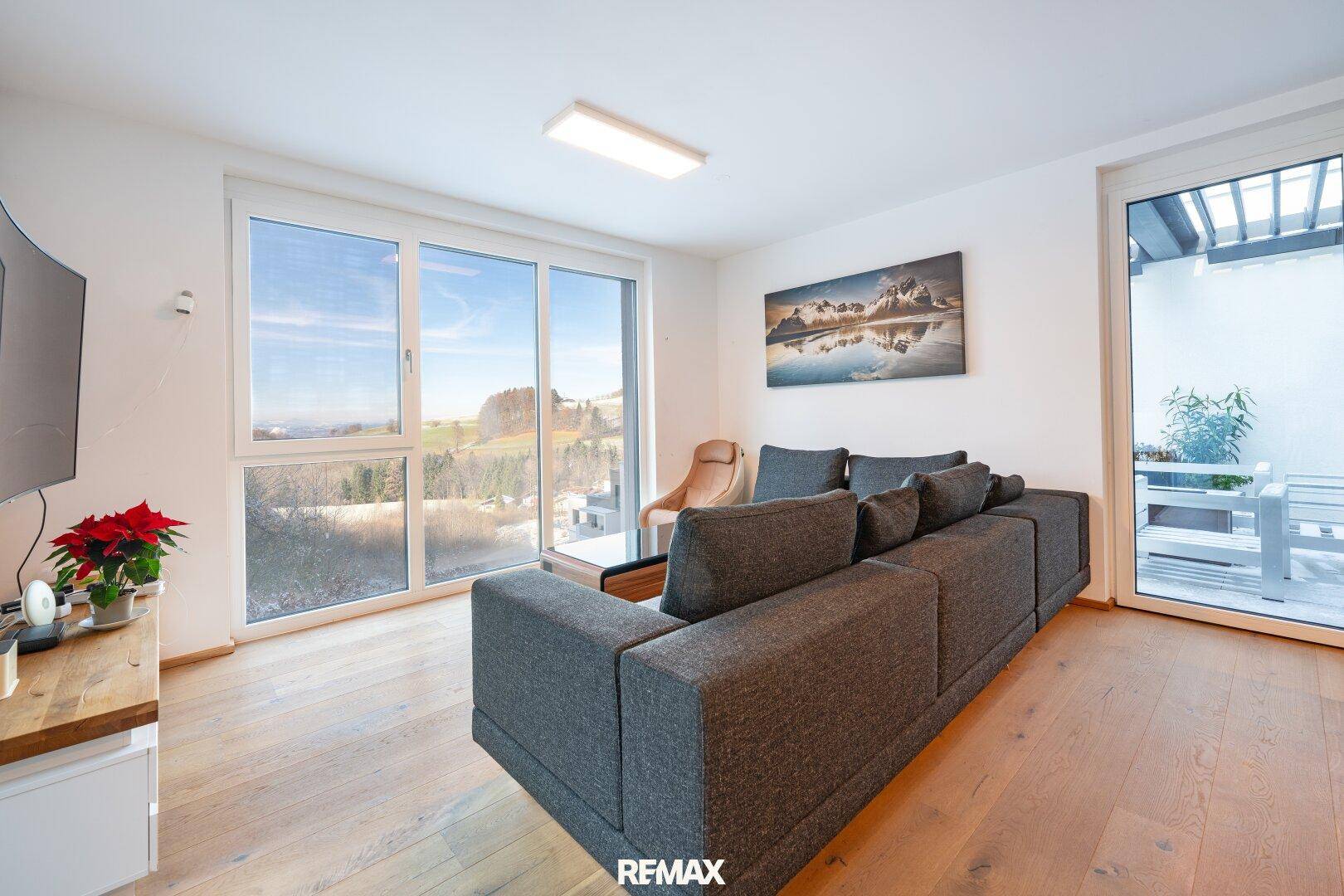Helles Wohnzimmer mit Holzboden, großem Sofa und Zugang zu einer Terrasse mit Weitblick.