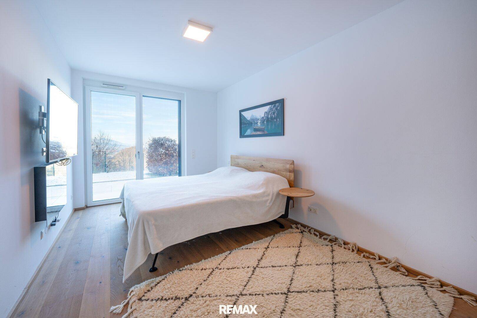 Helles Schlafzimmer mit Holzboden, großem Fenster und Zugang zu einem Außenbereich.
