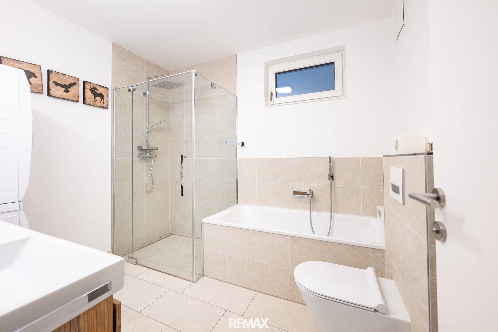 Modernes Badezimmer mit Badewanne, Duschkabine, WC und Fenster für Tageslicht.