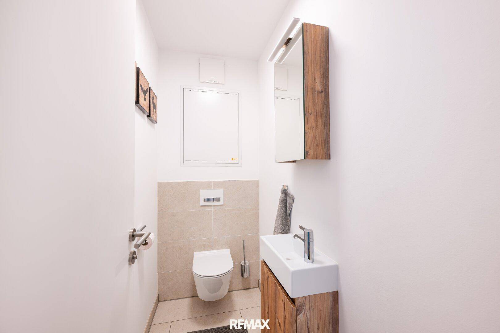 Separates Gäste-WC mit wandhängender Toilette, kleinem Waschbecken und Spiegelschrank.