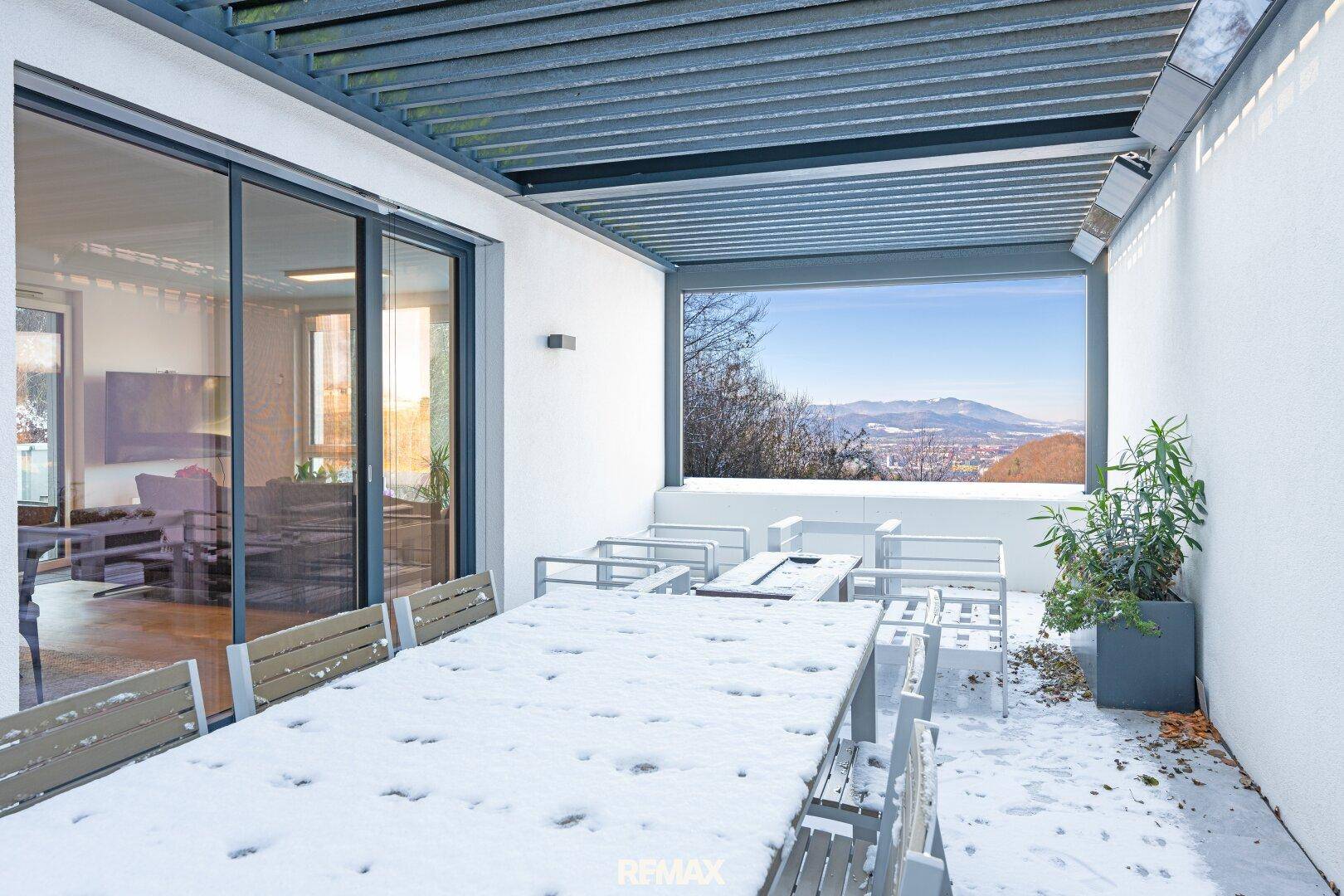 Überdachte Terrasse mit Esstisch und Stühlen, bedeckt mit Schnee und Weitblick.