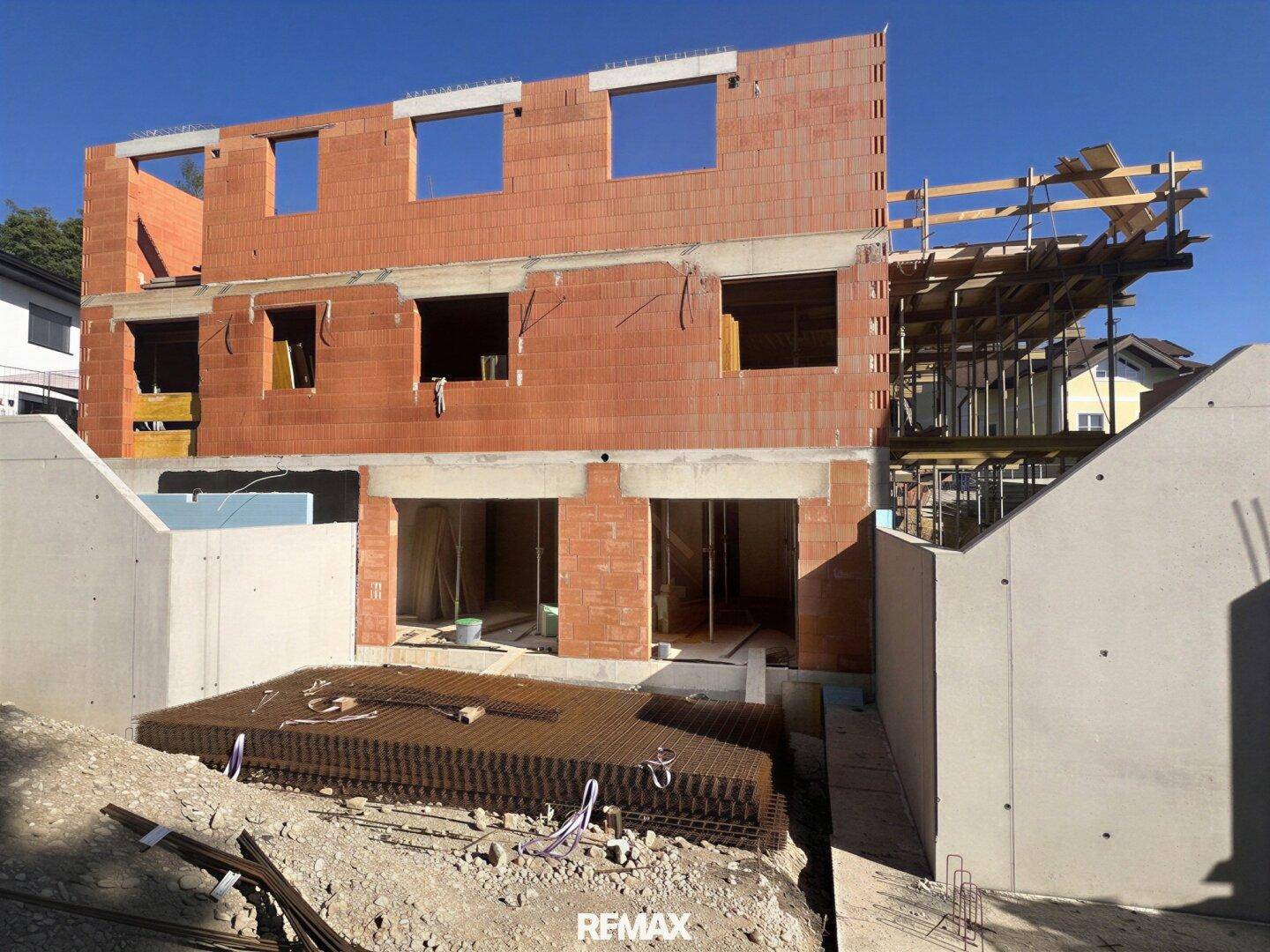 Neubau im Rohbau mit Ziegelwänden und Betonfundament unter blauem Himmel.