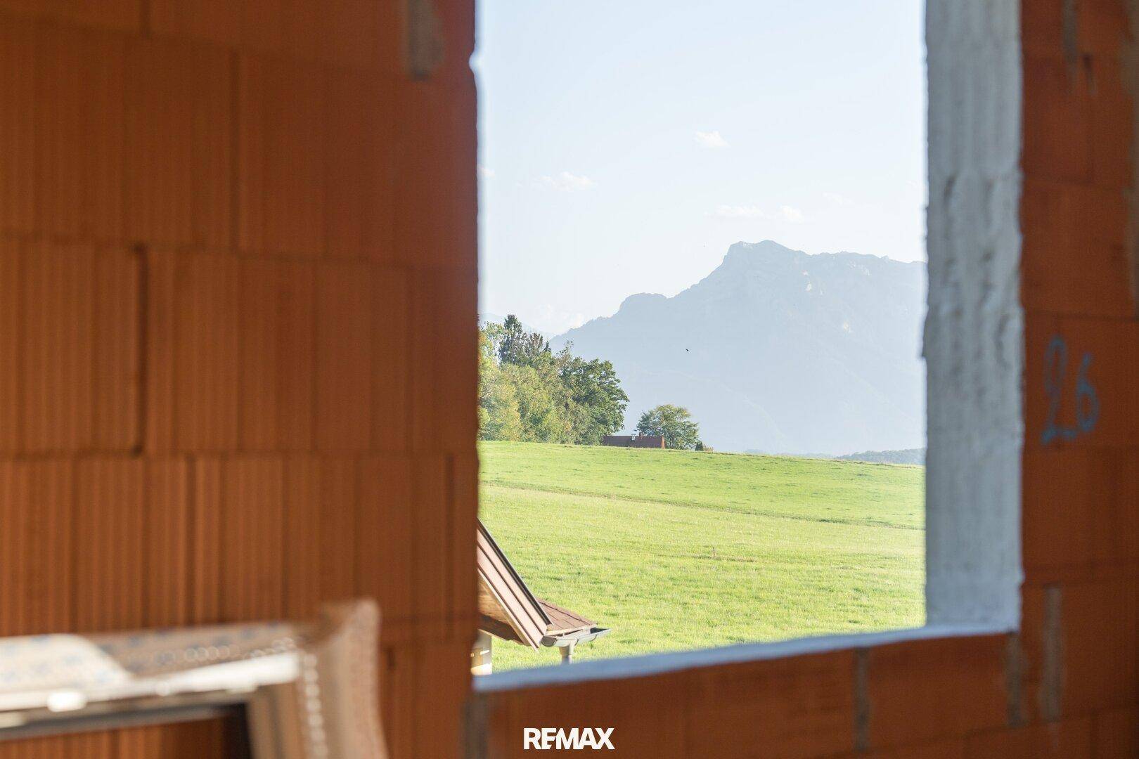 Blick durch eine Fensteröffnung in einer Ziegelwand auf eine grüne Wiese und ferne Berge.