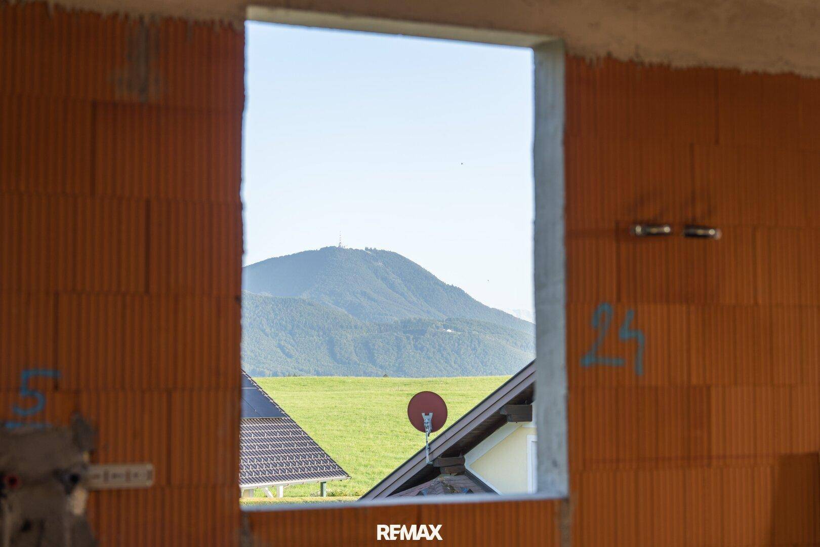 Fensterblick aus einem Rohbau auf eine weite grüne Landschaft mit einem Hügel im Hintergrund.