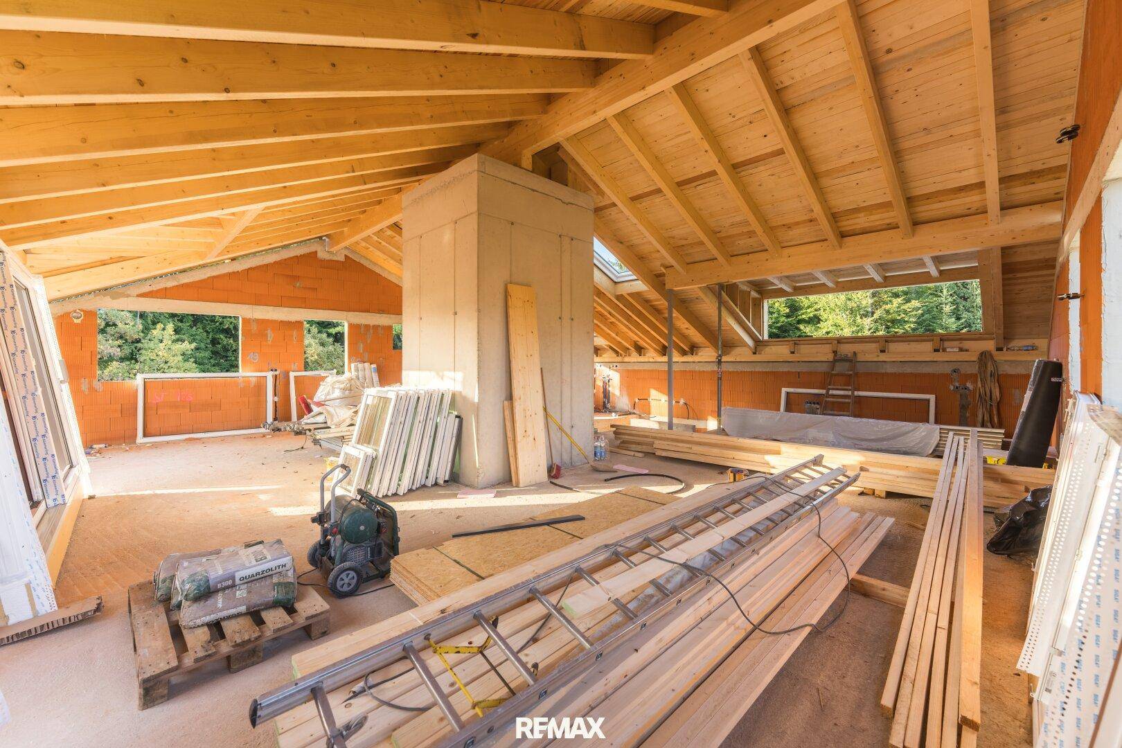 Innenansicht eines im Bau befindlichen Raumes mit sichtbaren Holzbalken und Ziegelwänden.