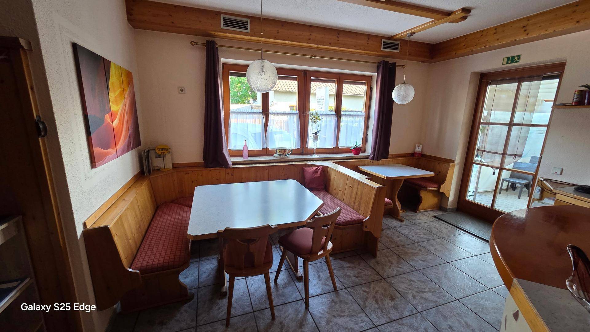 Heller Essbereich mit Eckbank, Holztischen und großen Fenstern, die viel Tageslicht hereinlassen.