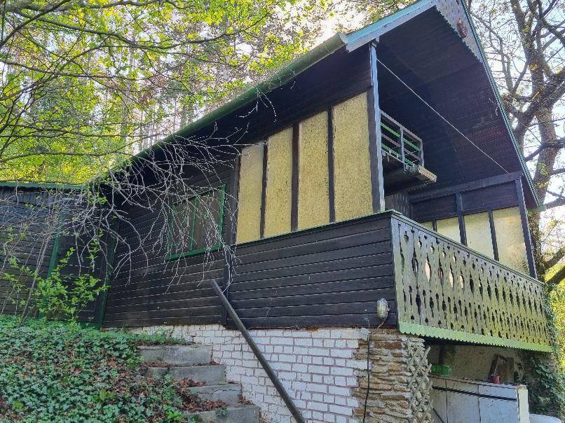 Traditionelles Holzhaus mit Balkon und gemauerter Basis, eingebettet in grüne Umgebung.