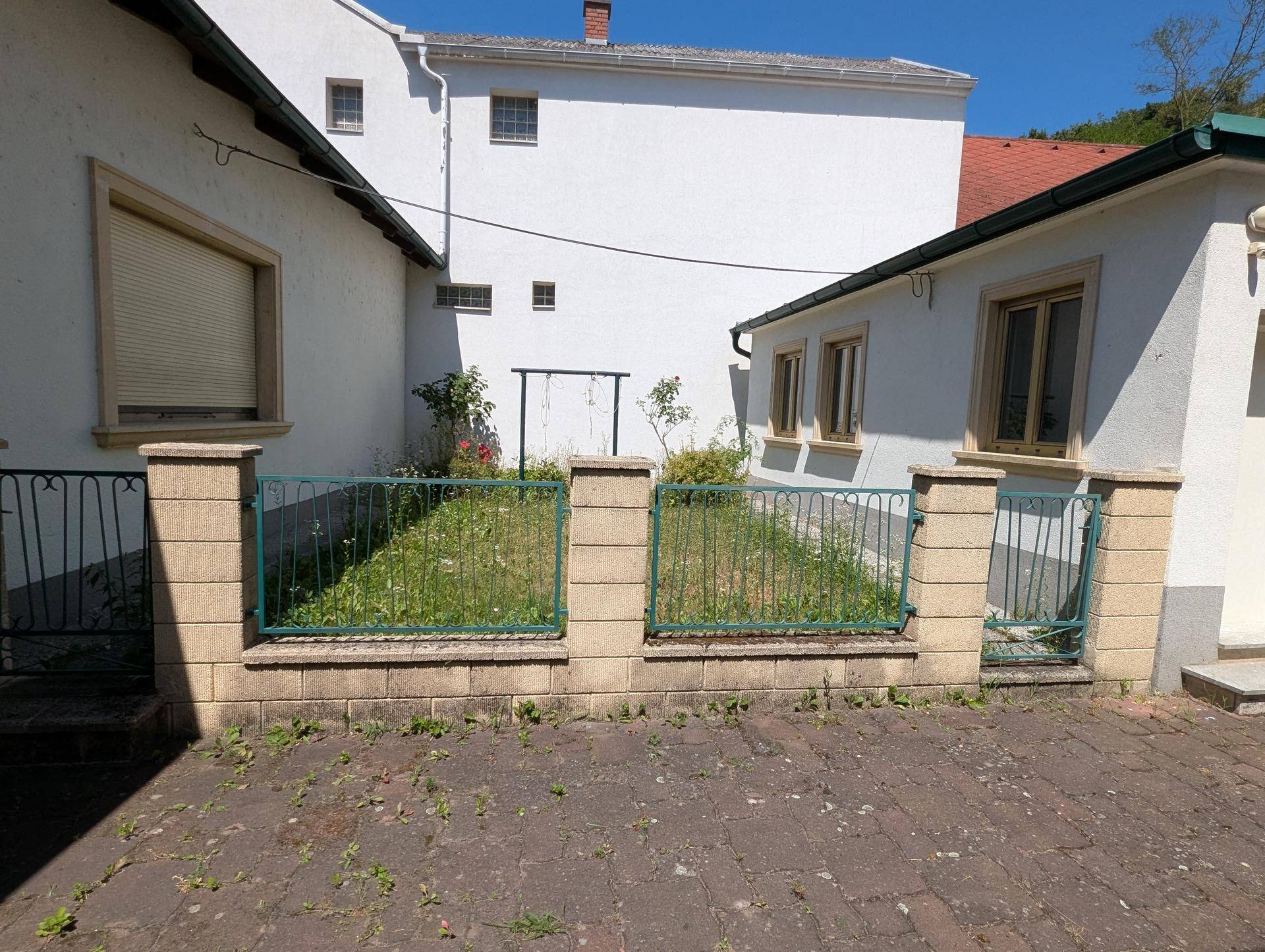 Kleiner Gartenbereich mit Zaun und gepflastertem Vorplatz zwischen Gebäuden.