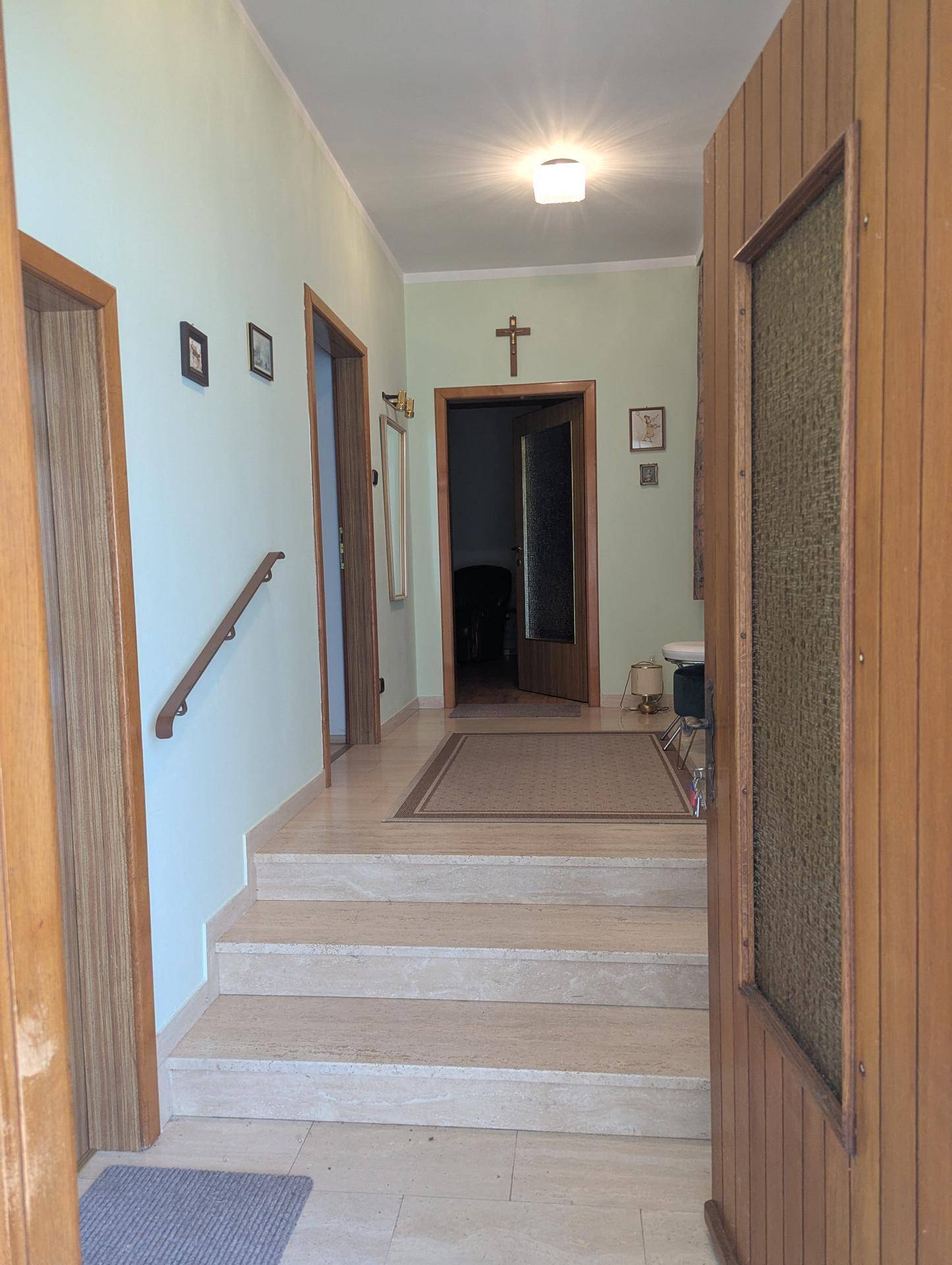 Heller Flur mit Treppe, Holzvertäfelung und religiöser Dekoration.