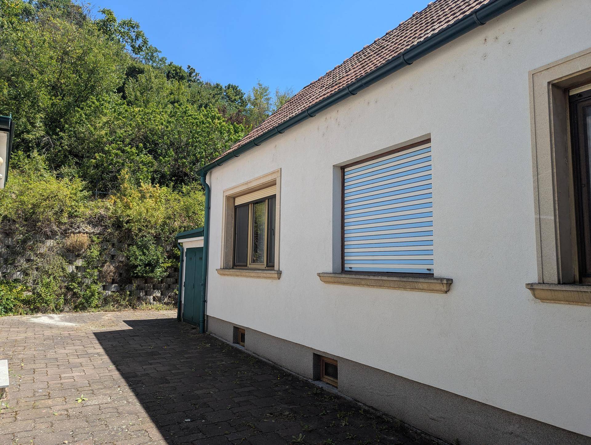 Seitenansicht eines Hauses mit Fenstern, Rollläden und Ziegeldach.