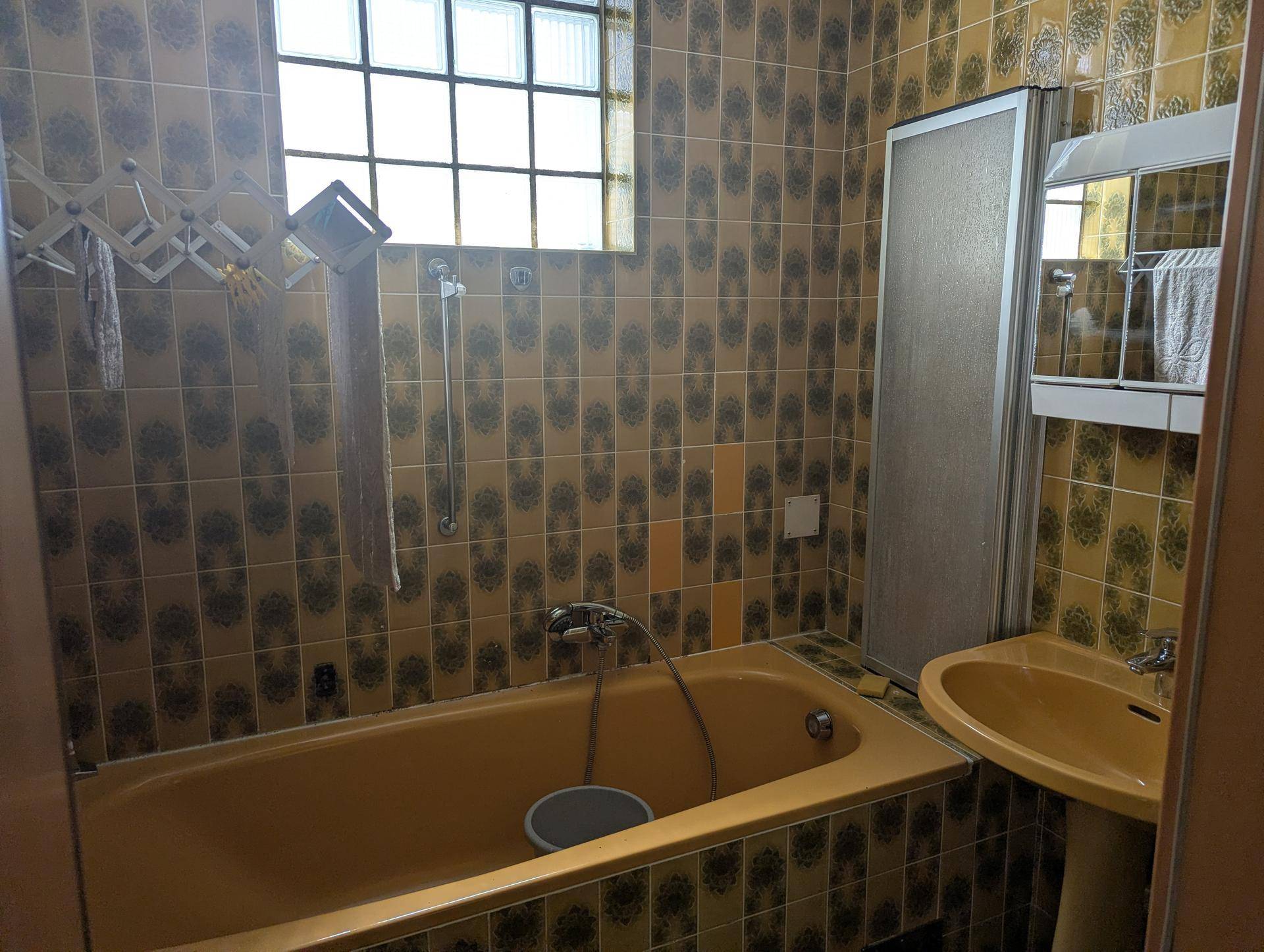 Badezimmer mit gelber Badewanne, Duschkabine und gemusterten Fliesen.