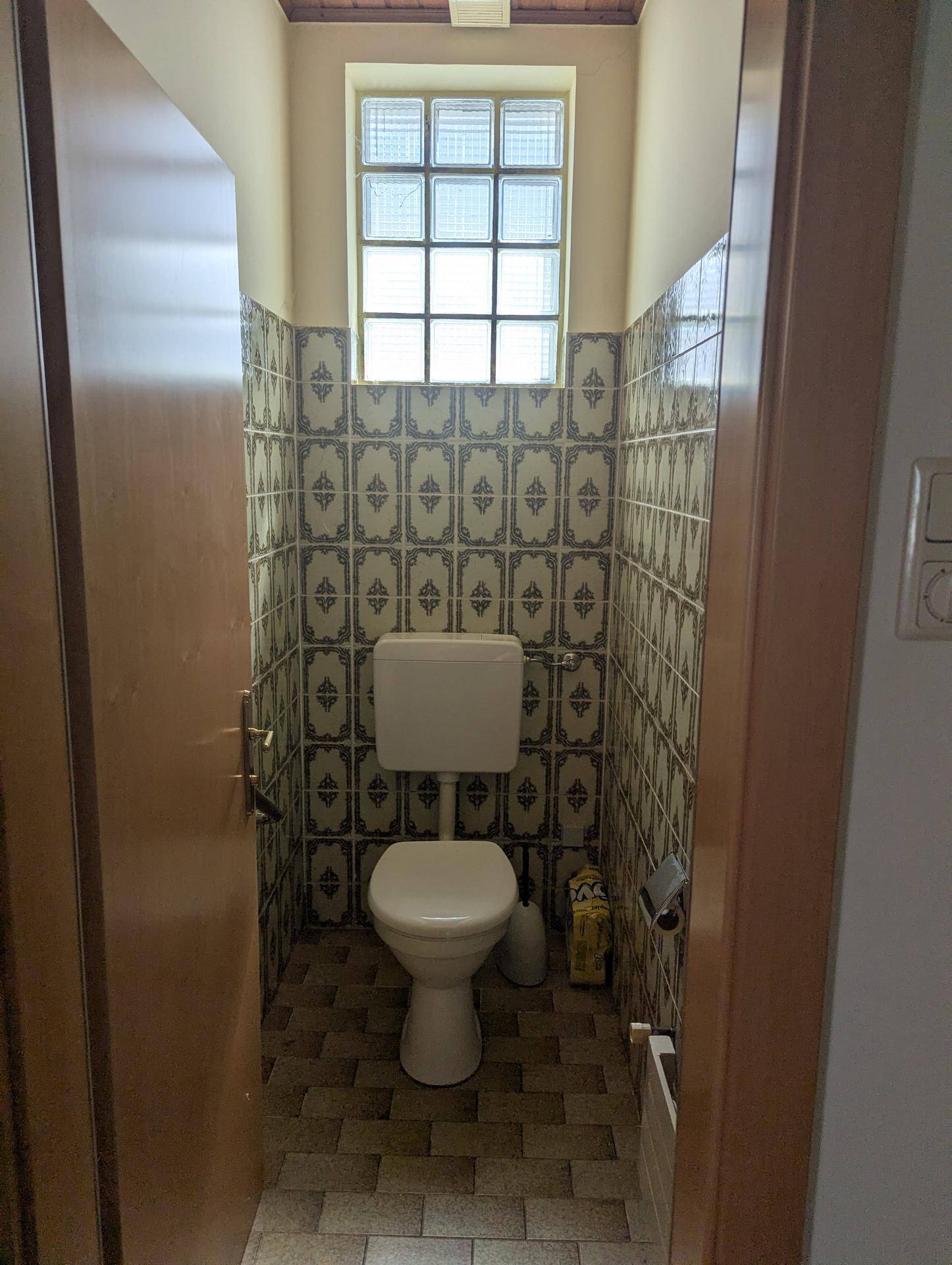 Kleines WC mit gemusterten Fliesen und Fenster aus Glasbausteinen.