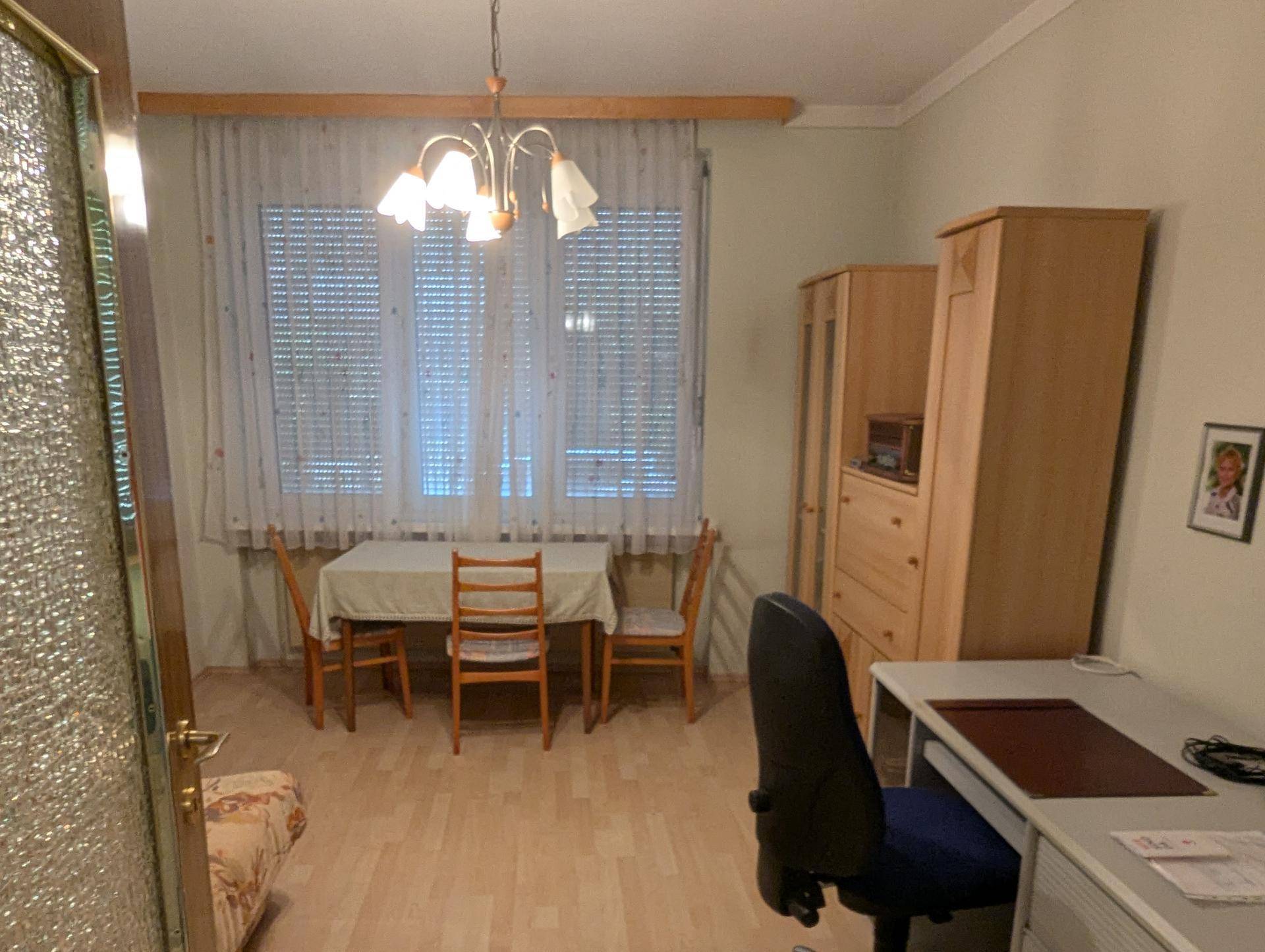 Zimmer mit Esstisch, Schreibtisch und Fenster mit Rollläden.