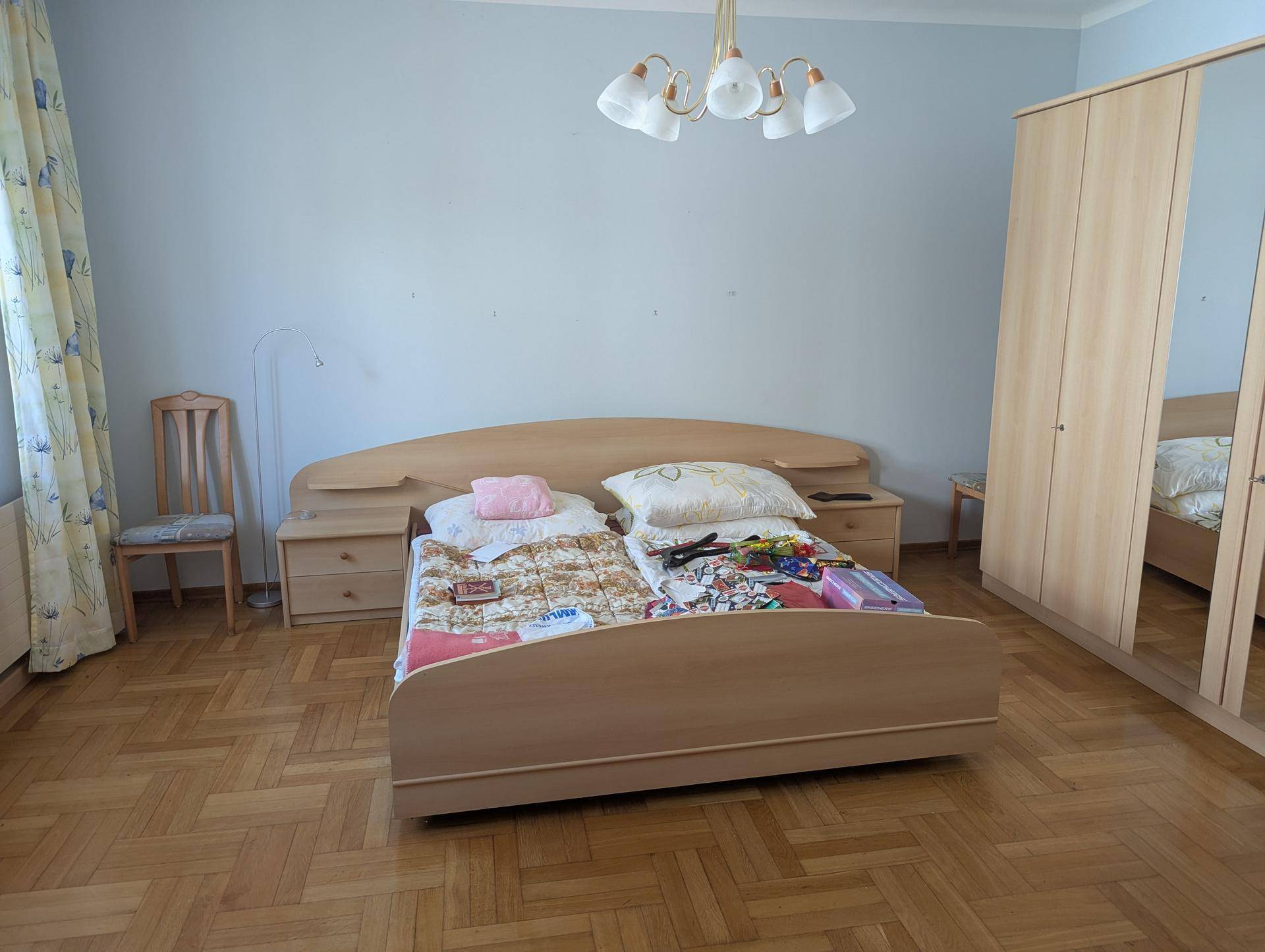 Schlafzimmer mit Doppelbett, Holzschrank und Fischgrätparkettboden.