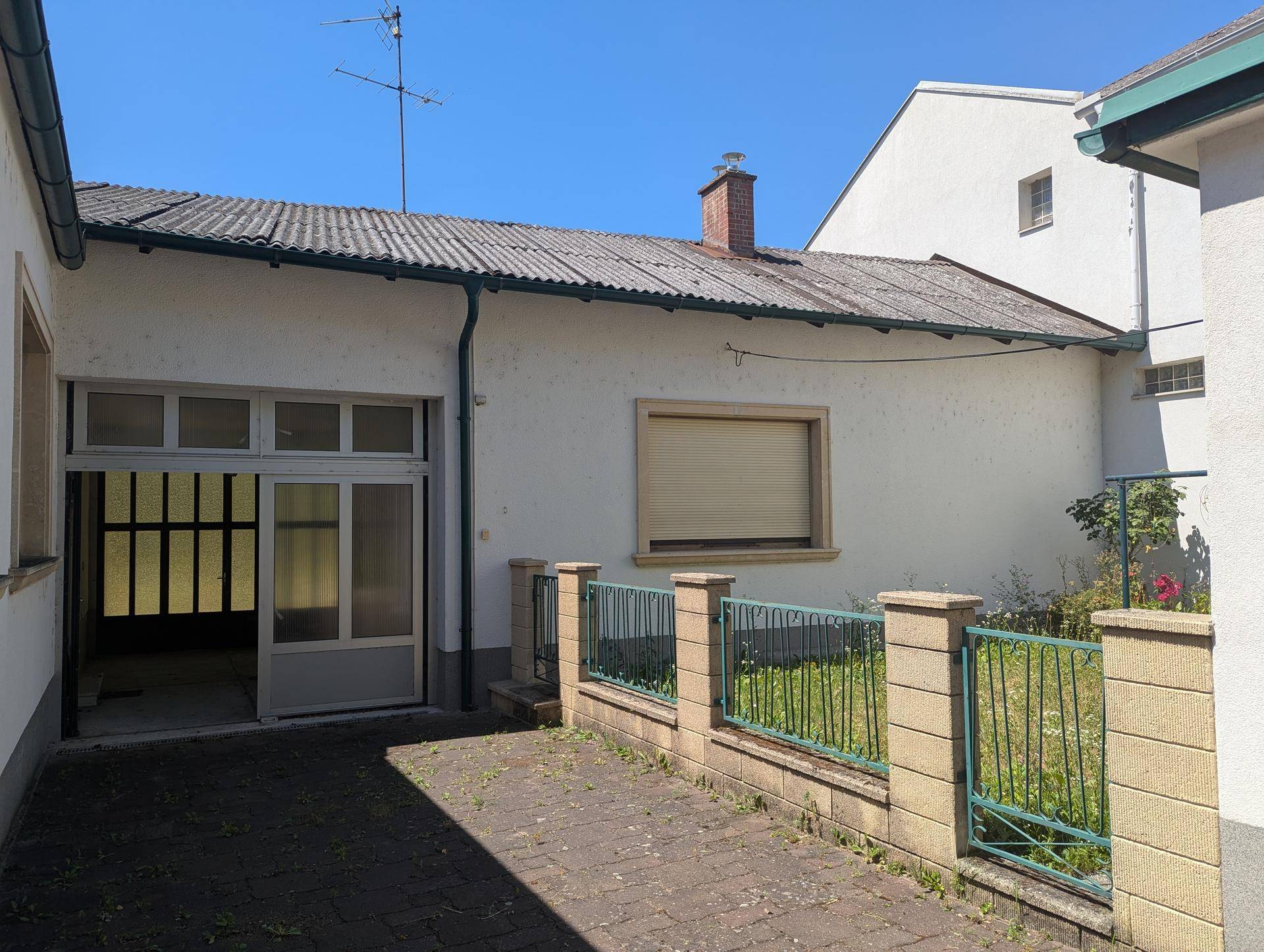 Rückseite des Gebäudes mit Garagenzugang und kleinem, eingezäunten Gartenbereich.