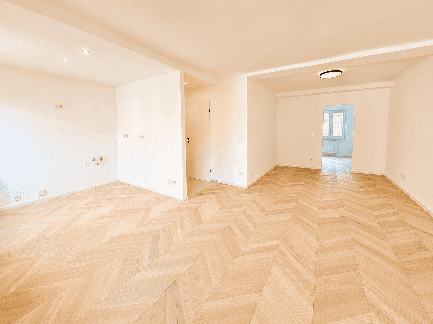 Weitläufiger Wohnbereich mit Fischgrätparkett und Blick in angrenzende Zimmer.
