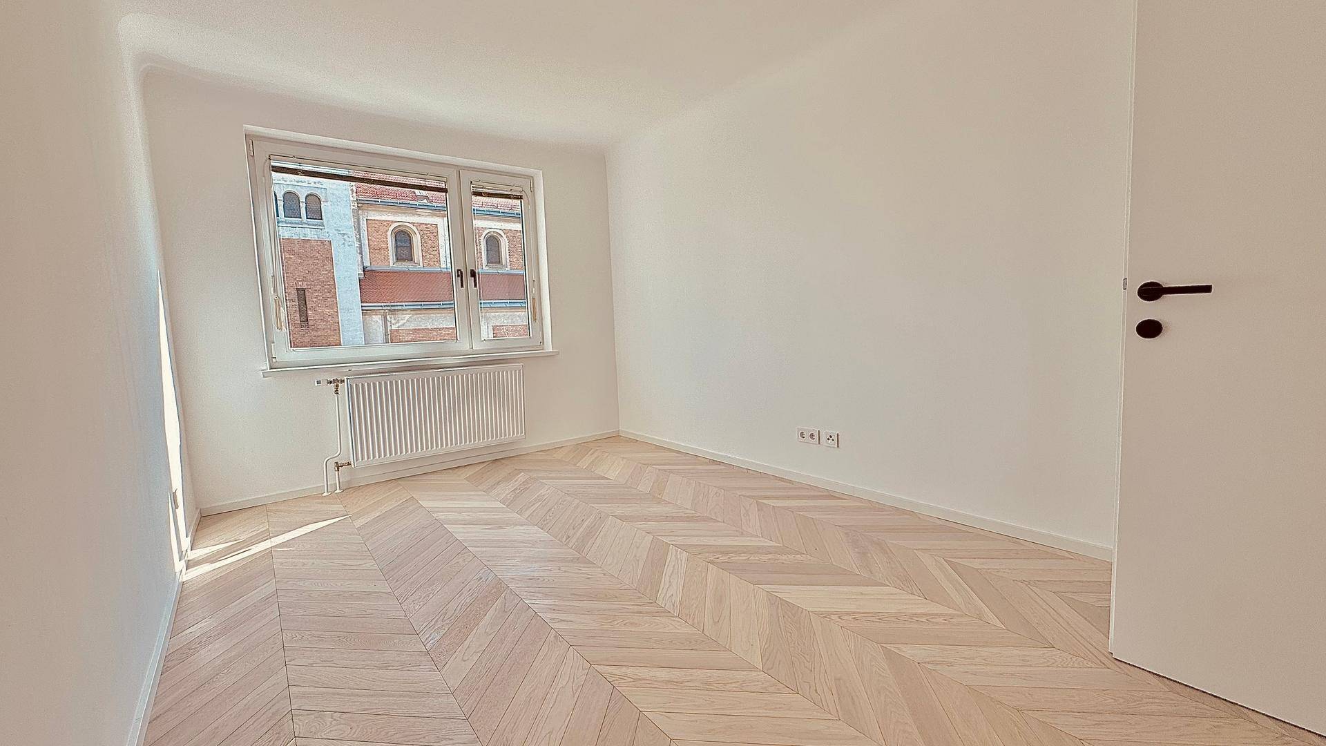 Helles Schlafzimmer mit Fischgrätparkett und einem Fenster mit Blick auf die Stadt.