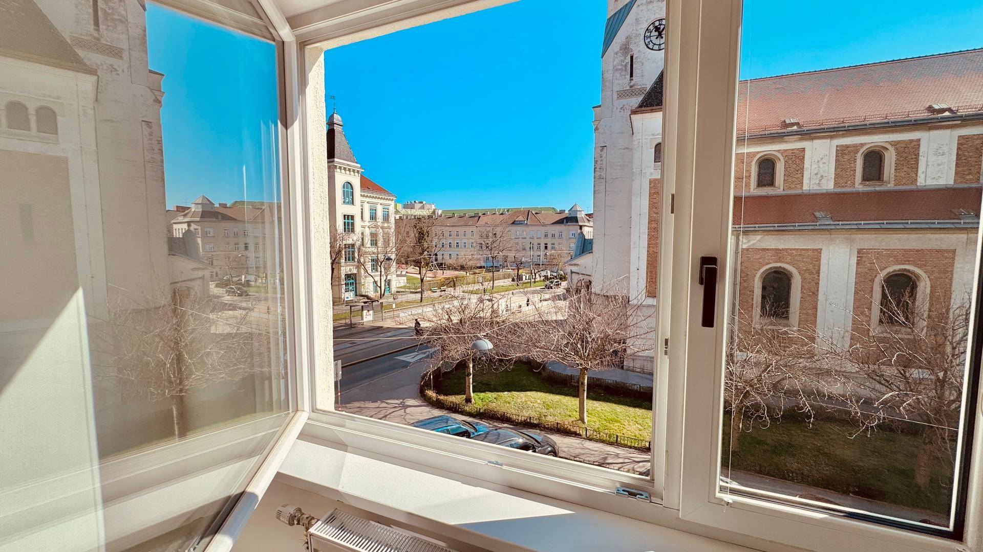 Blick aus dem Fenster auf eine belebte Stadtstraße mit historischen Gebäuden und einem Park.
