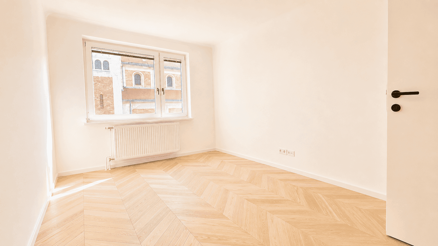 Helles Schlafzimmer mit Fischgrätparkett, großem Fenster und Blick auf die Umgebung.