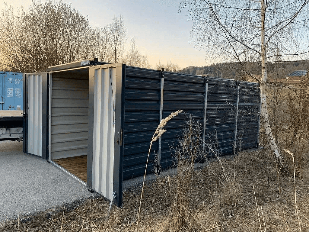Lagercontainer mit geöffneten Türen in einer ländlichen Umgebung mit Bäumen und Sträuchern.
