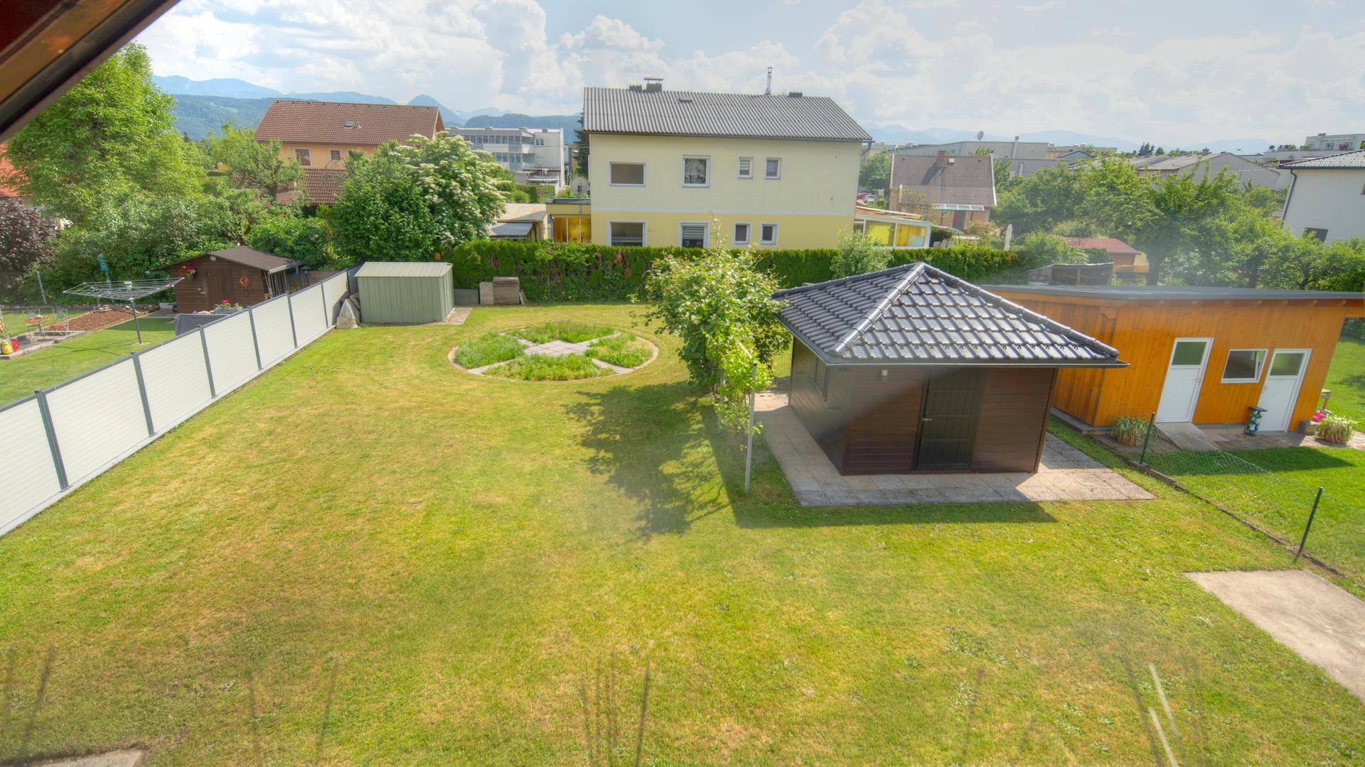 Weitläufiger Garten mit Rasen, Gartenhaus und Blick auf die umliegende Landschaft und Berge.