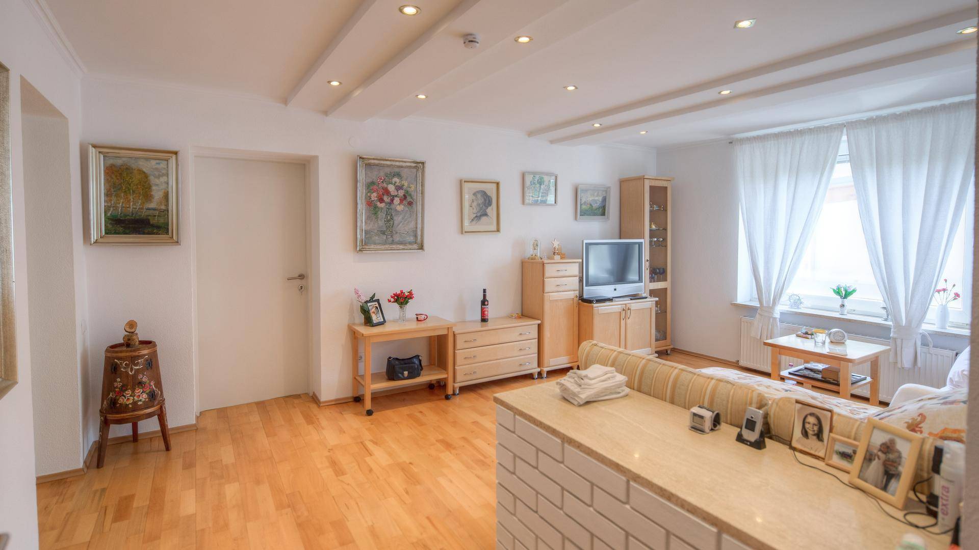 Geräumiges Wohnzimmer mit Holzboden, Deckenstrahlern und Blick auf den grünen Garten.
