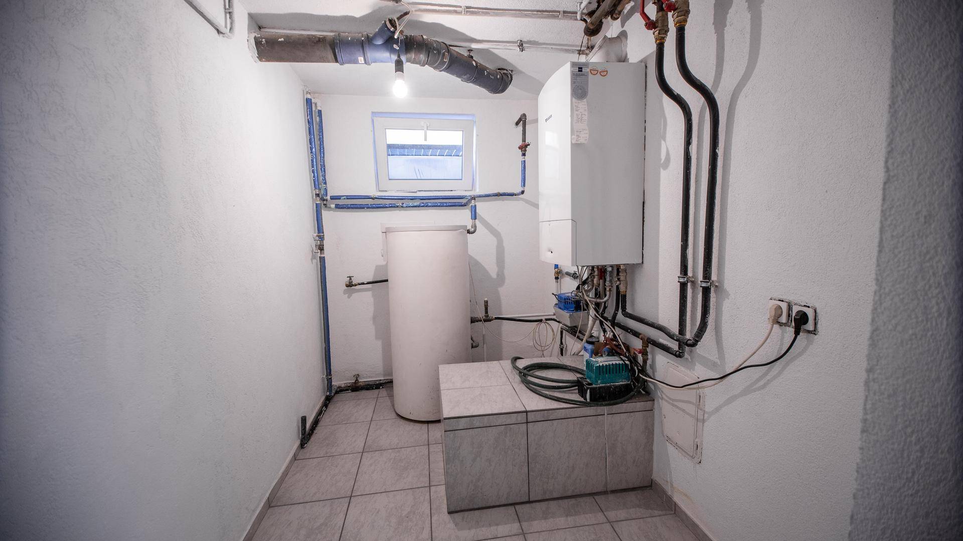 Heizungsraum im Keller mit Boiler, sichtbaren Rohren und kleinem Fenster für Belüftung.