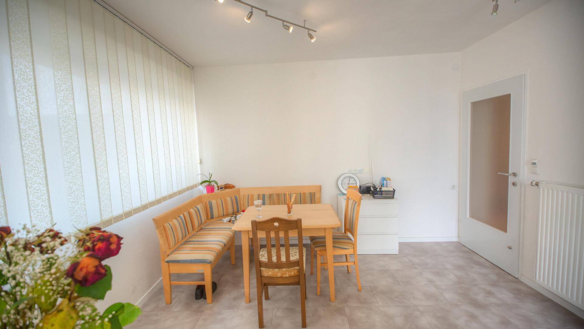 Heller Essbereich mit Holztisch, Eckbank und Stühlen, gefliestem Boden und Fenster.