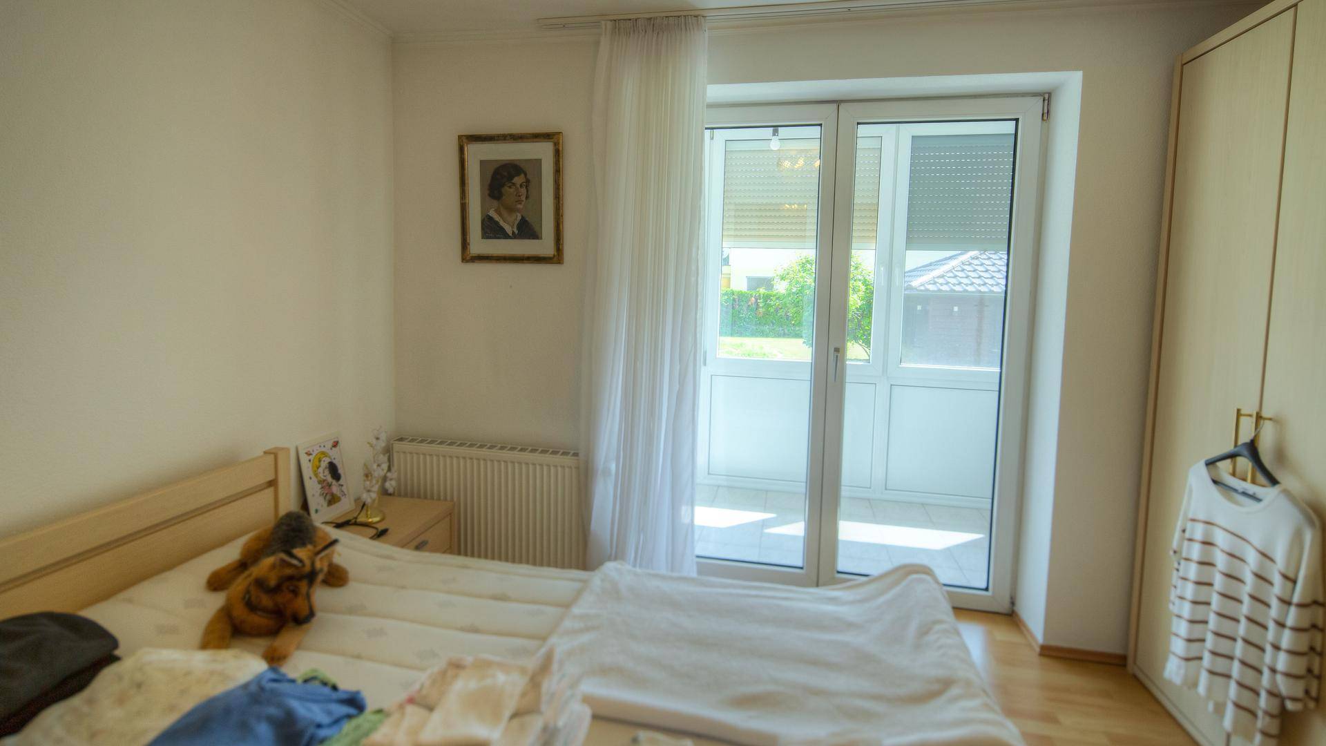Schlafzimmer mit Zugang zum Balkon, Holzboden und einem angenehmen Blick ins Grüne.