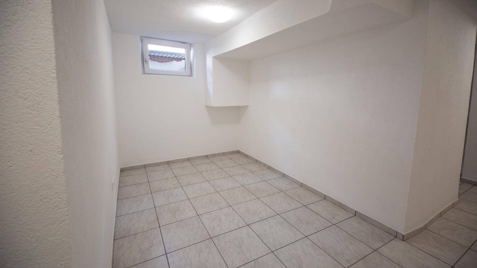 Geräumiger Kellerraum mit Fliesenboden und kleinem Fenster, vielseitig nutzbar.