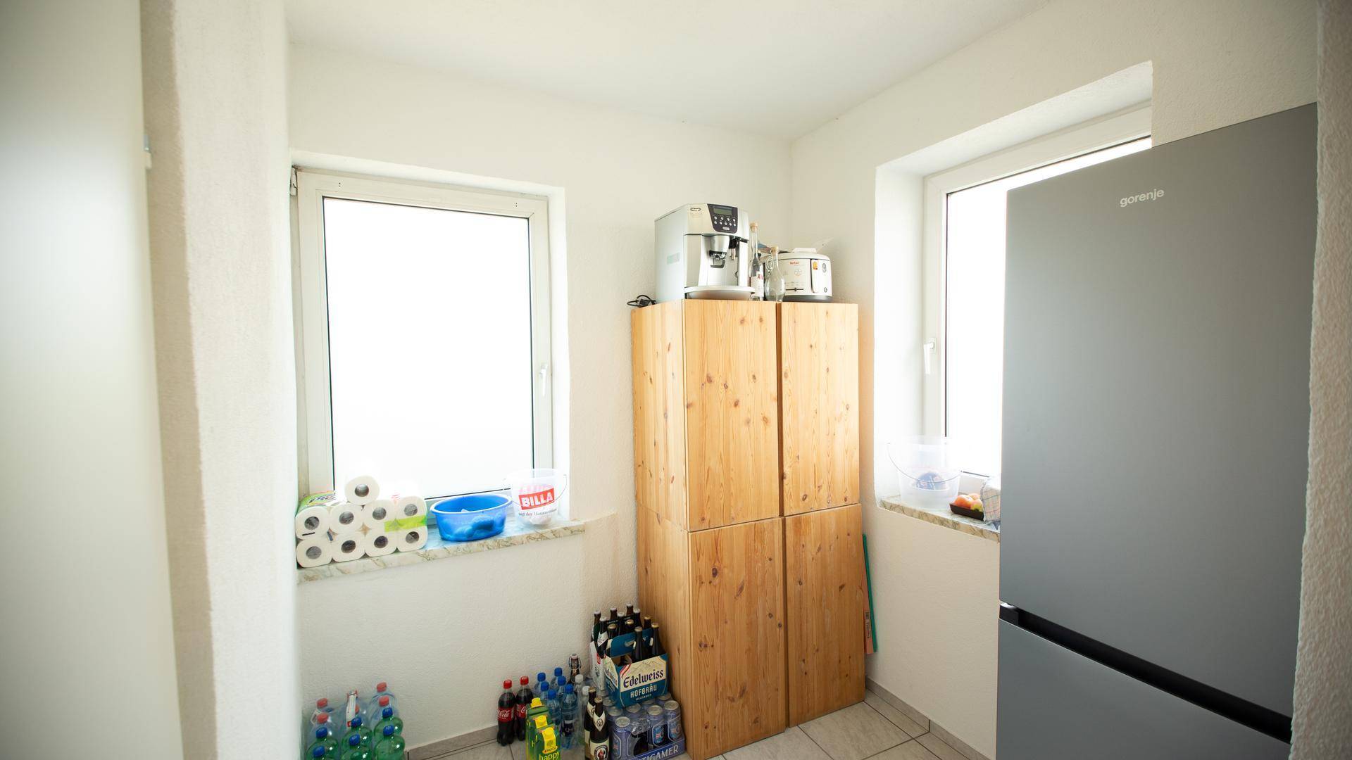 Heller Abstellraum mit Kühlschrank, Holzschränken und zwei Fenstern für Tageslicht.
